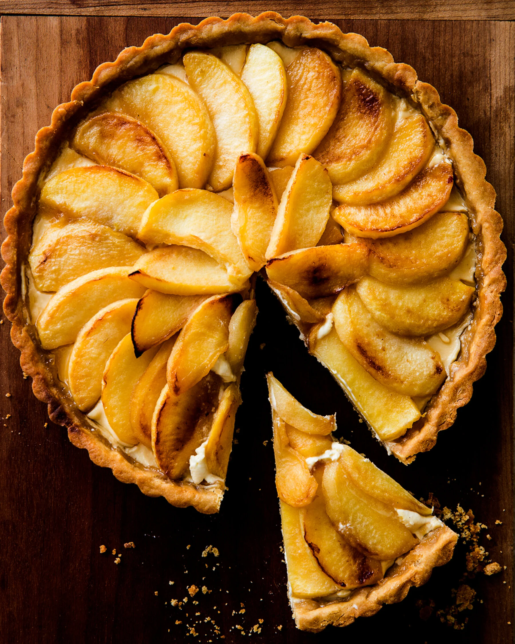 A sliced peach tart with a golden, flaky crust on a wooden surface. Boston based food and hospitality photographer.