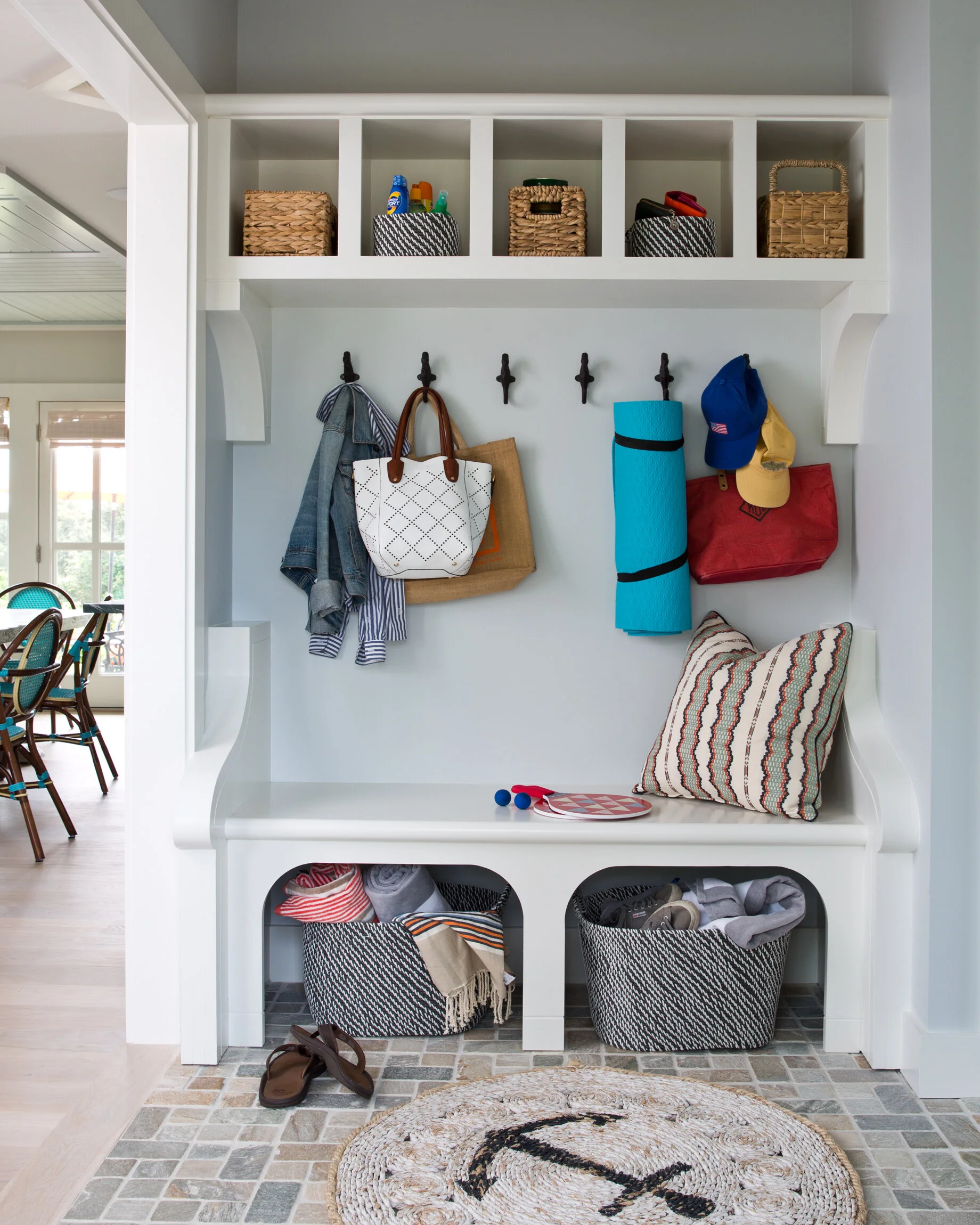 Entryway with hooks, baskets, bags, hats, rolled yoga mat, pillow, and storage baskets.