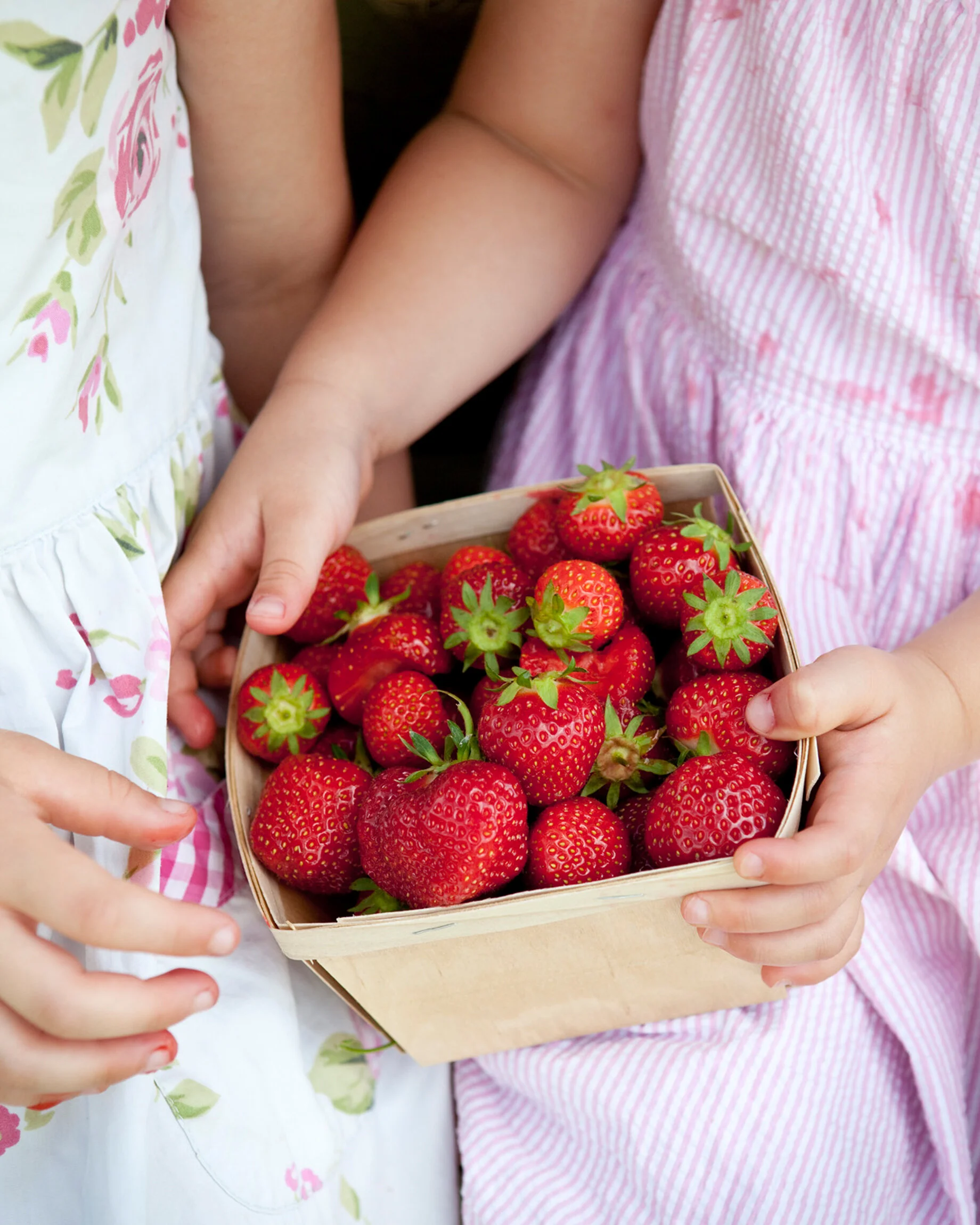 Two children holding a wooden basket filled with ripe strawberries.