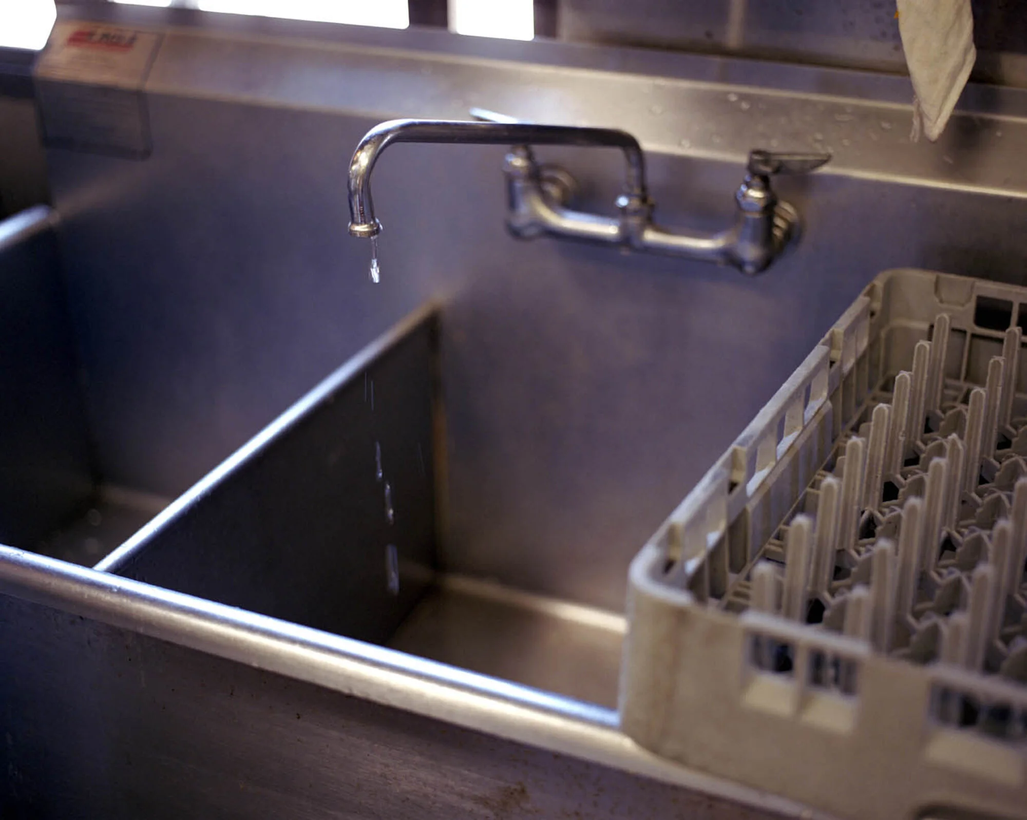 A stainless steel kitchen sink with a running faucet and a dish drying rack on the right side.