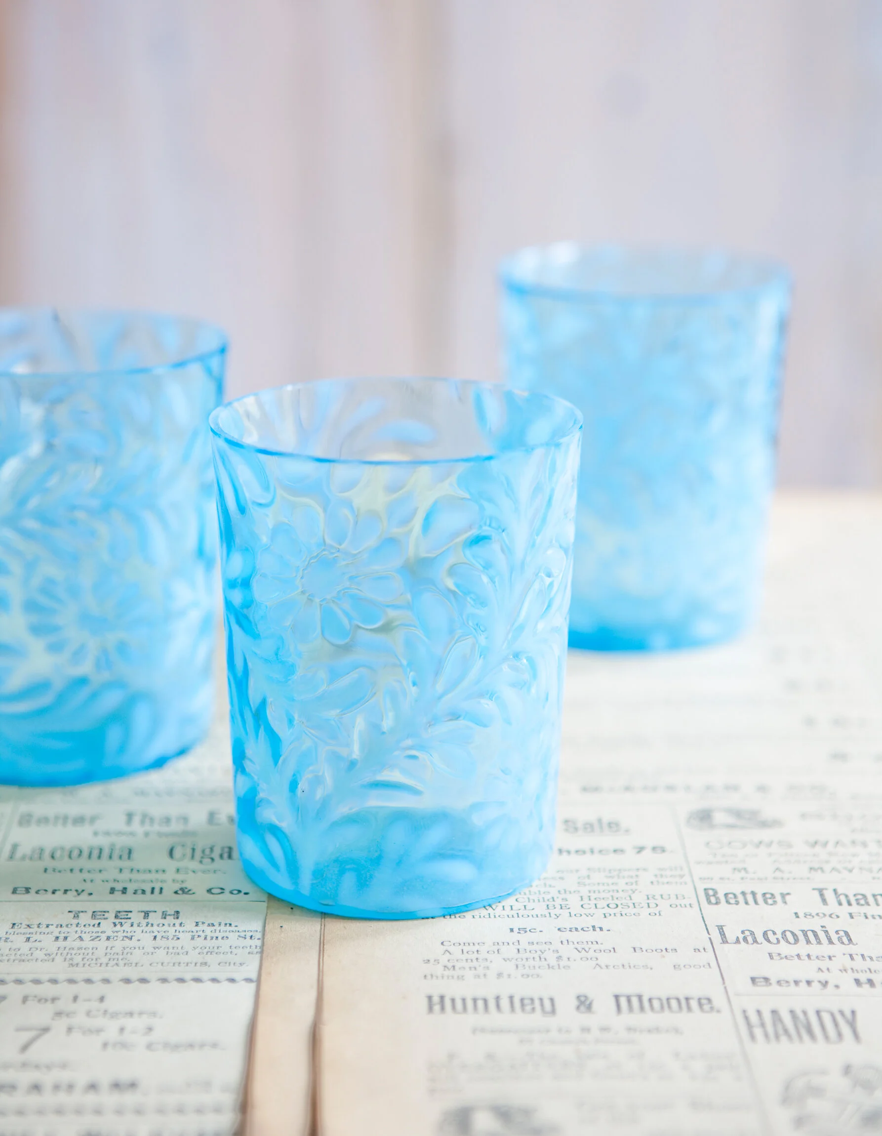 Three blue textured glass cups on a newspaper.