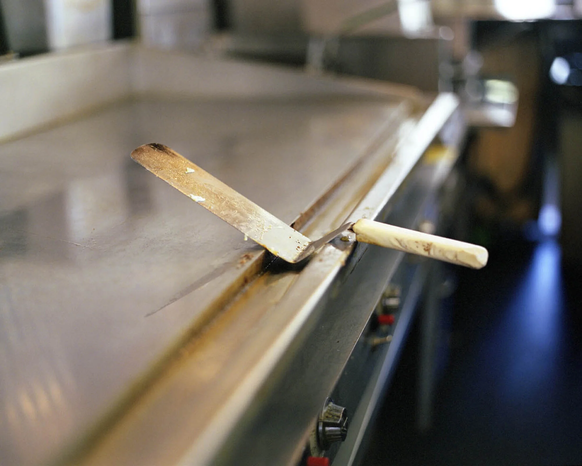 A pair of used spatulas resting on a stainless steel griddle in a commercial kitchen.