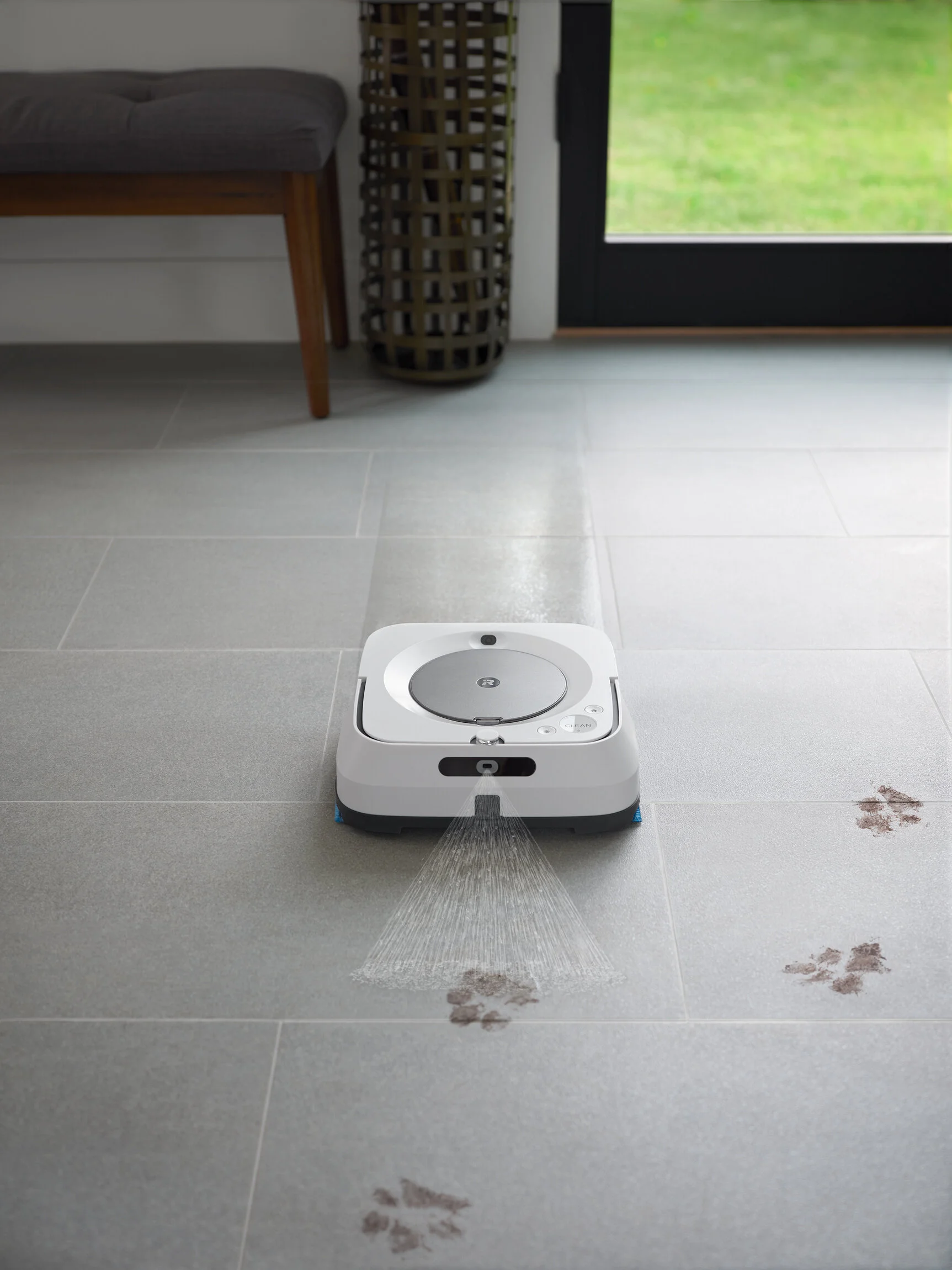 Robot vacuum cleaner cleaning dirt footprints on tiled floor near glass door. Photographed by Joseph Keller for iRobot