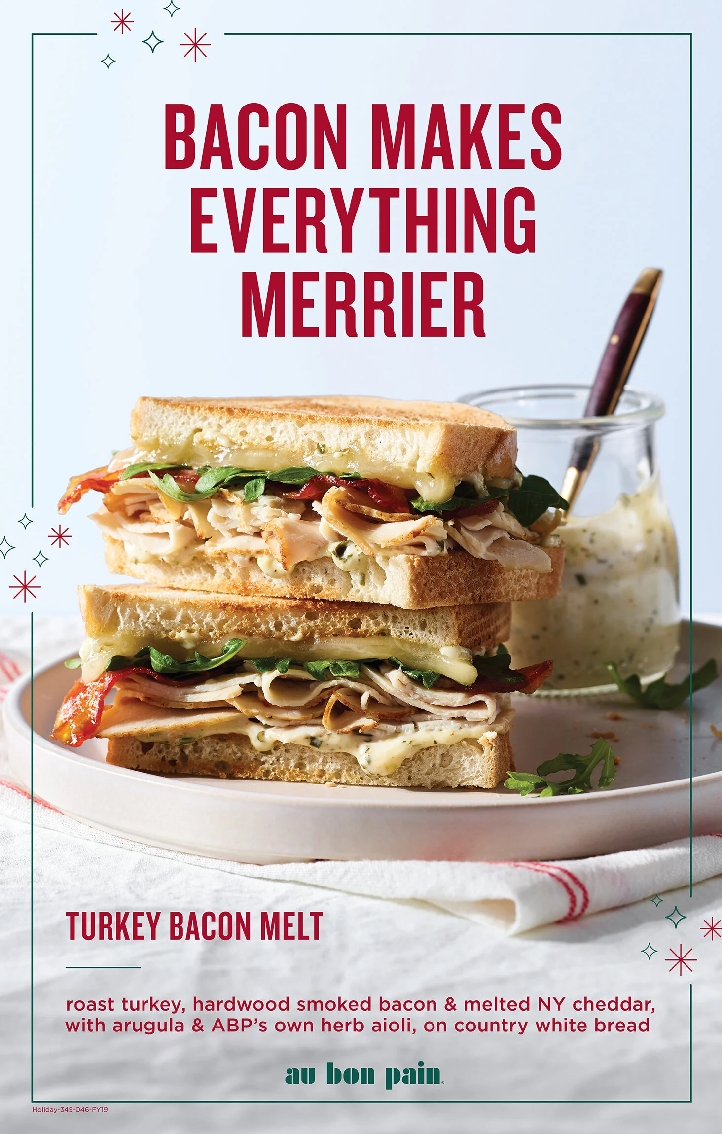 A sandwich with turkey and bacon on country white bread with greens and melted cheese, beside a jar of herbed aioli. The text reads "Bacon makes everything merrier" and describes a turkey bacon melt sandwich. In-Store poster for Au Bon Pain Cafe