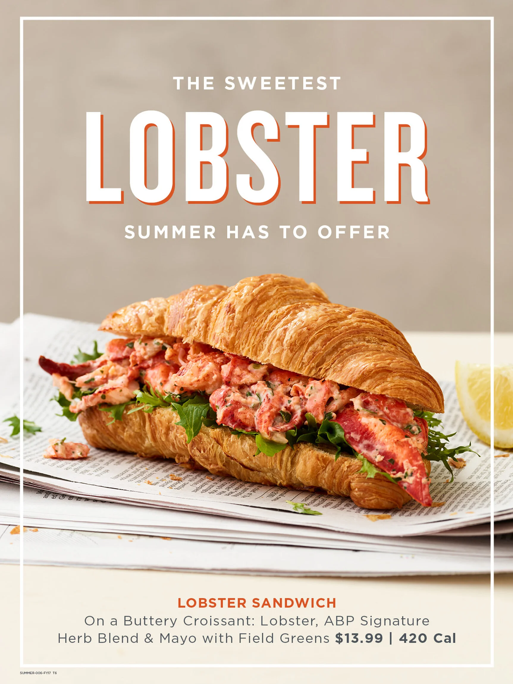 Lobster sandwich on a croissant with lettuce, lemon wedge in the background, on a newspaper. In store poster for Au Bon Pain Cafe