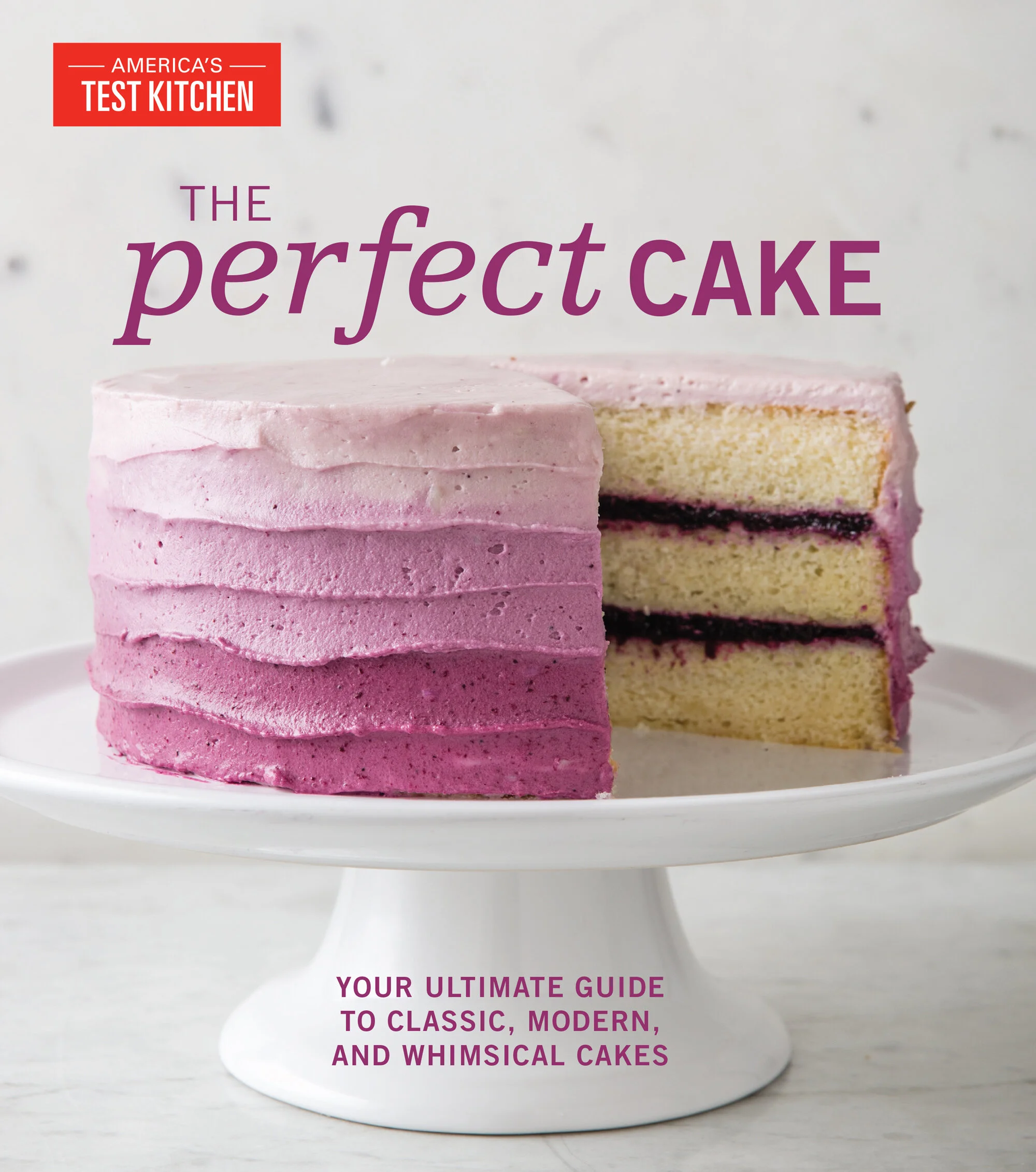 Cover of the cookbook, The Perfect Cake by Americas Test Kitchen. A layered pink cake with frosting on a white cake stand, with a slice cut out showing cream filling and layers, on a white background.