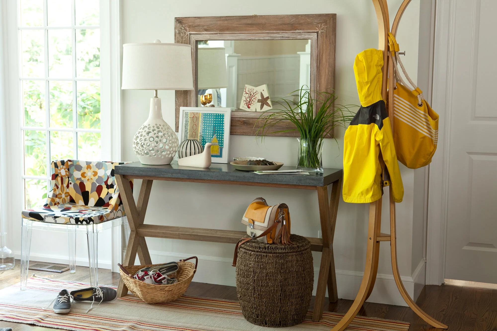 Entryway with console table, mirror, colorful chair, yellow raincoat, yellow bag, basket with shoes, and decorative items.