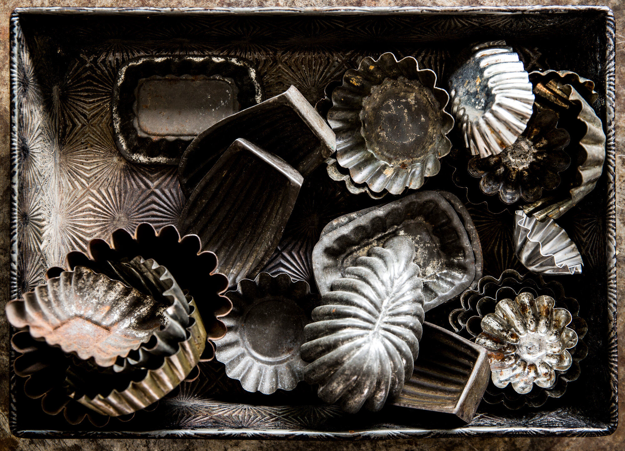 A collection of vintage metal baking molds and tart tins in various shapes and sizes in a metal tray.