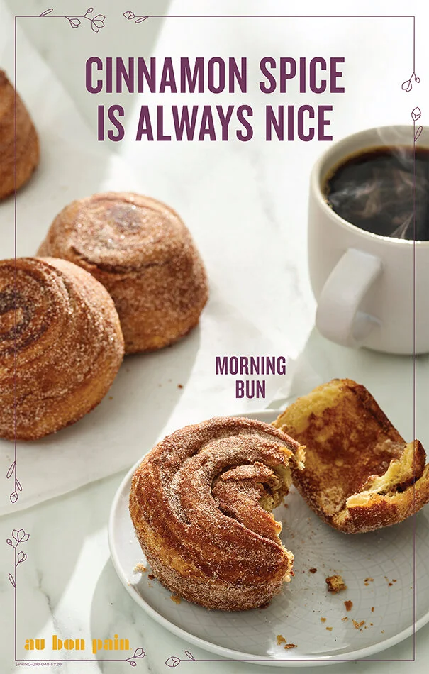Cinnamon rolls, sugar-coated, on a white plate with one partly eaten roll, next to a cup of black coffee, with a softened white background and decorative purple borders, and the text "Cinnamon Spice Is Always Nice" in purple at the top, and "Morning 
