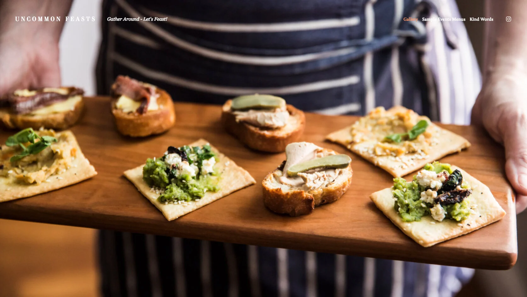 Person holding a wooden tray with assorted savory crackers topped with cheeses, vegetables, and garnishes.