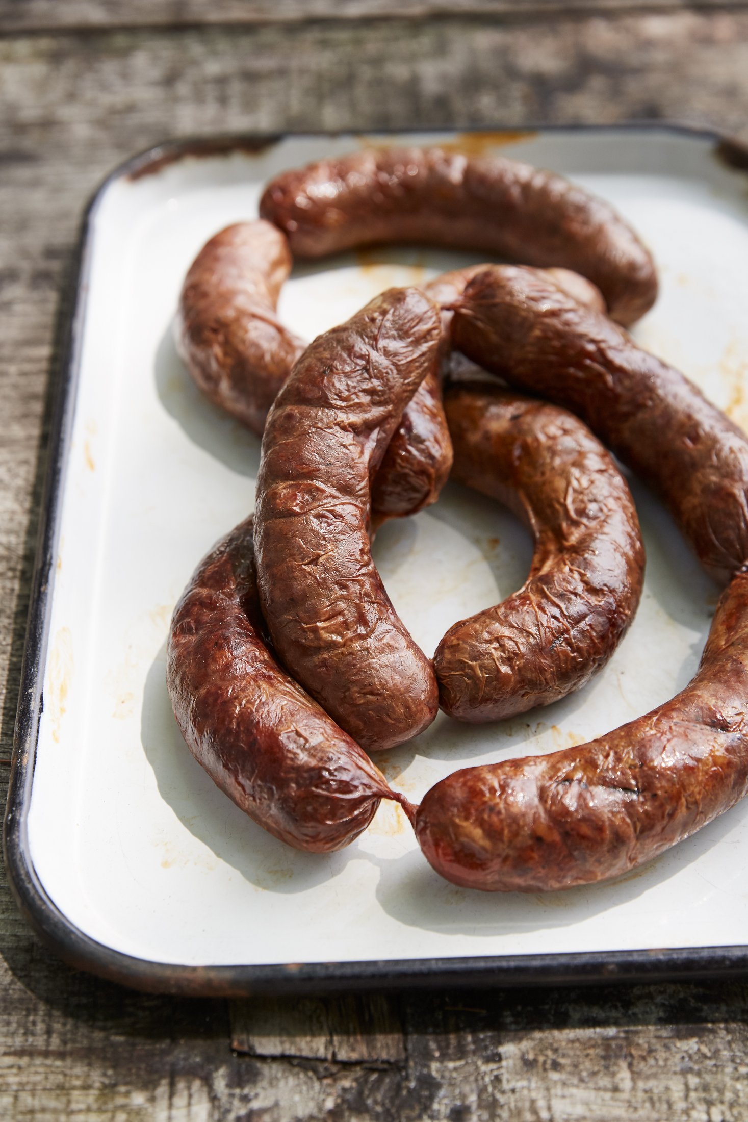 Cooked sausages on a white enamel tray on a wooden surface.