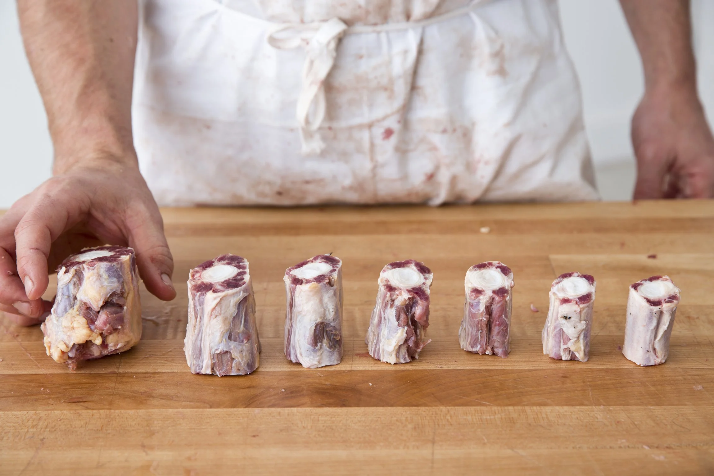 A person is preparing beef short ribs by cutting them into smaller pieces on a wooden cutting board.