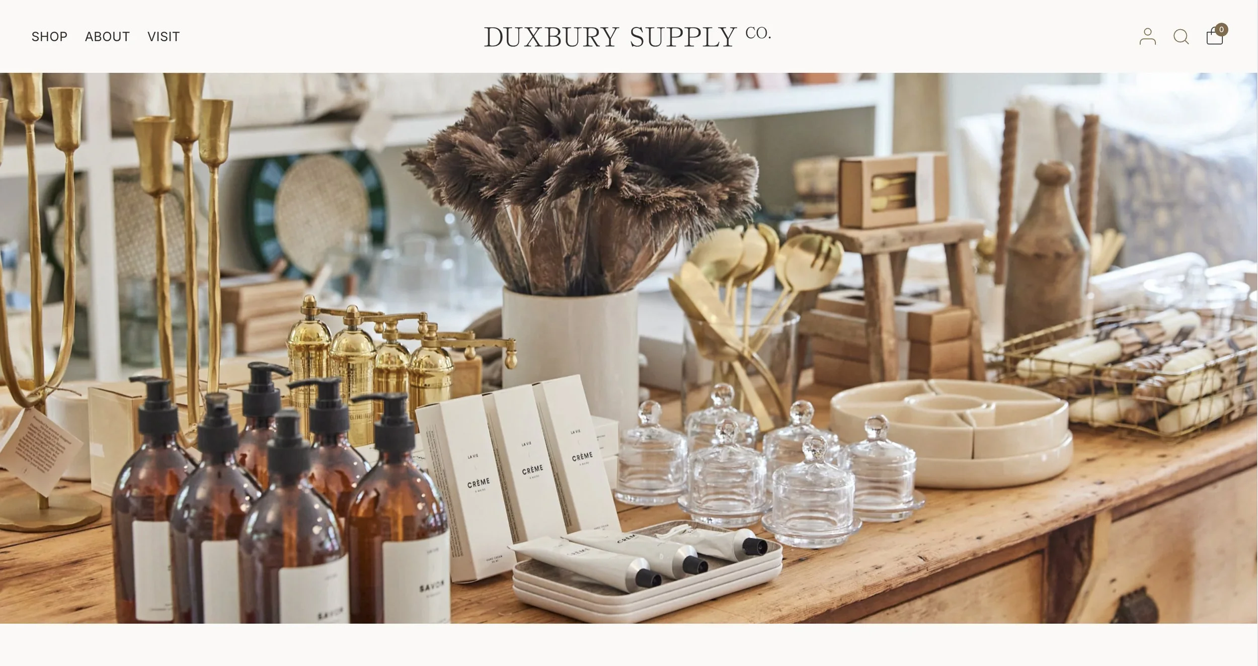 Display of home decor and bathroom accessories including soap dispensers, creams, glass jars, and decorative items on a wooden table. Screenshot of Duxbury Supply Co's web site