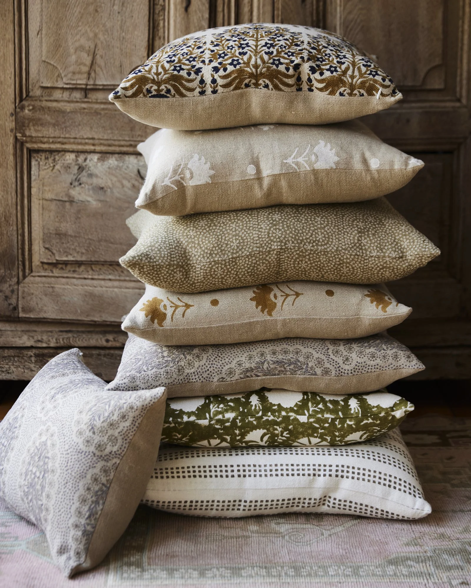 Stack of designer pillows against a rustic antique cabinet.