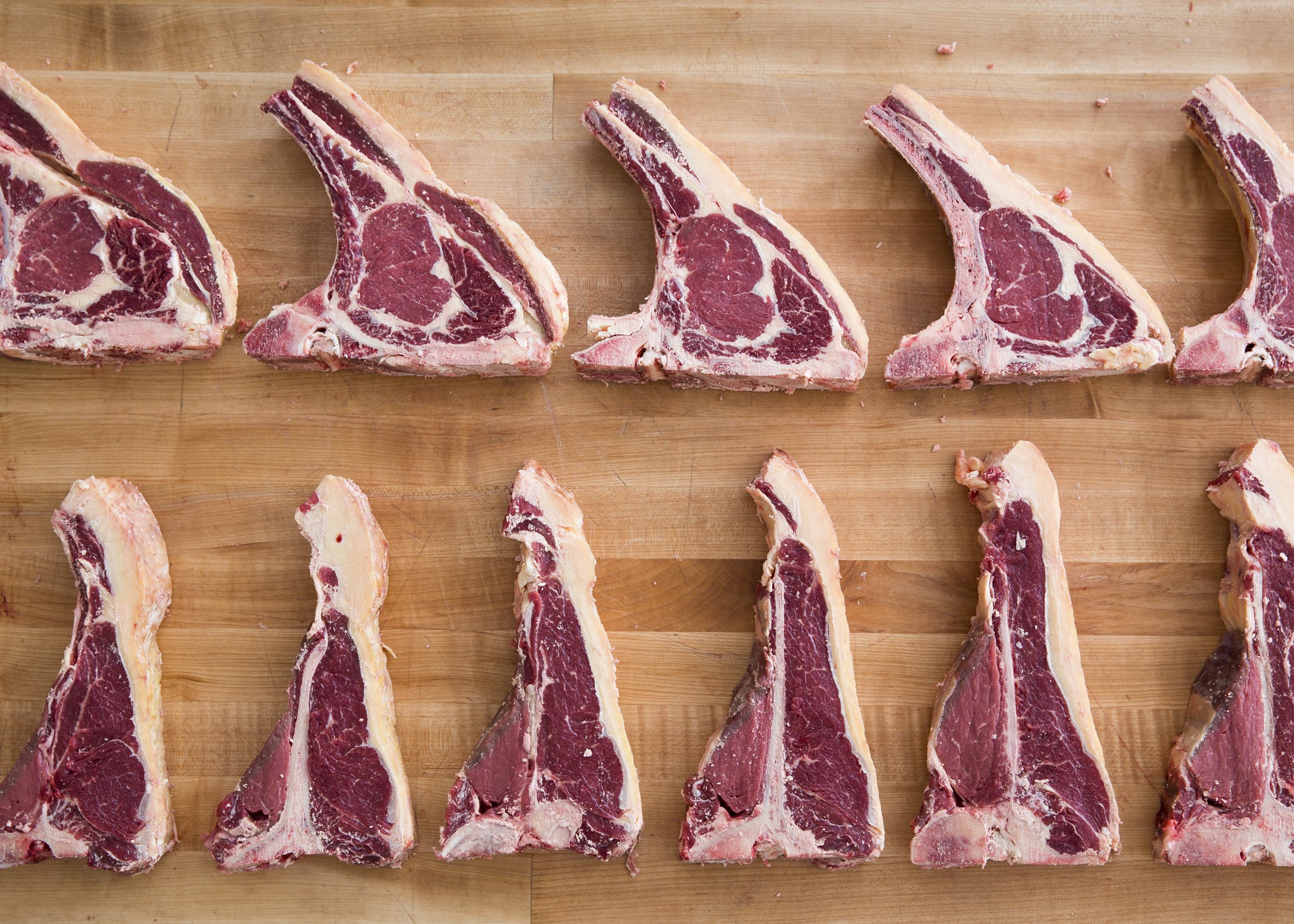 Several raw beef short ribs placed on a wooden cutting board.