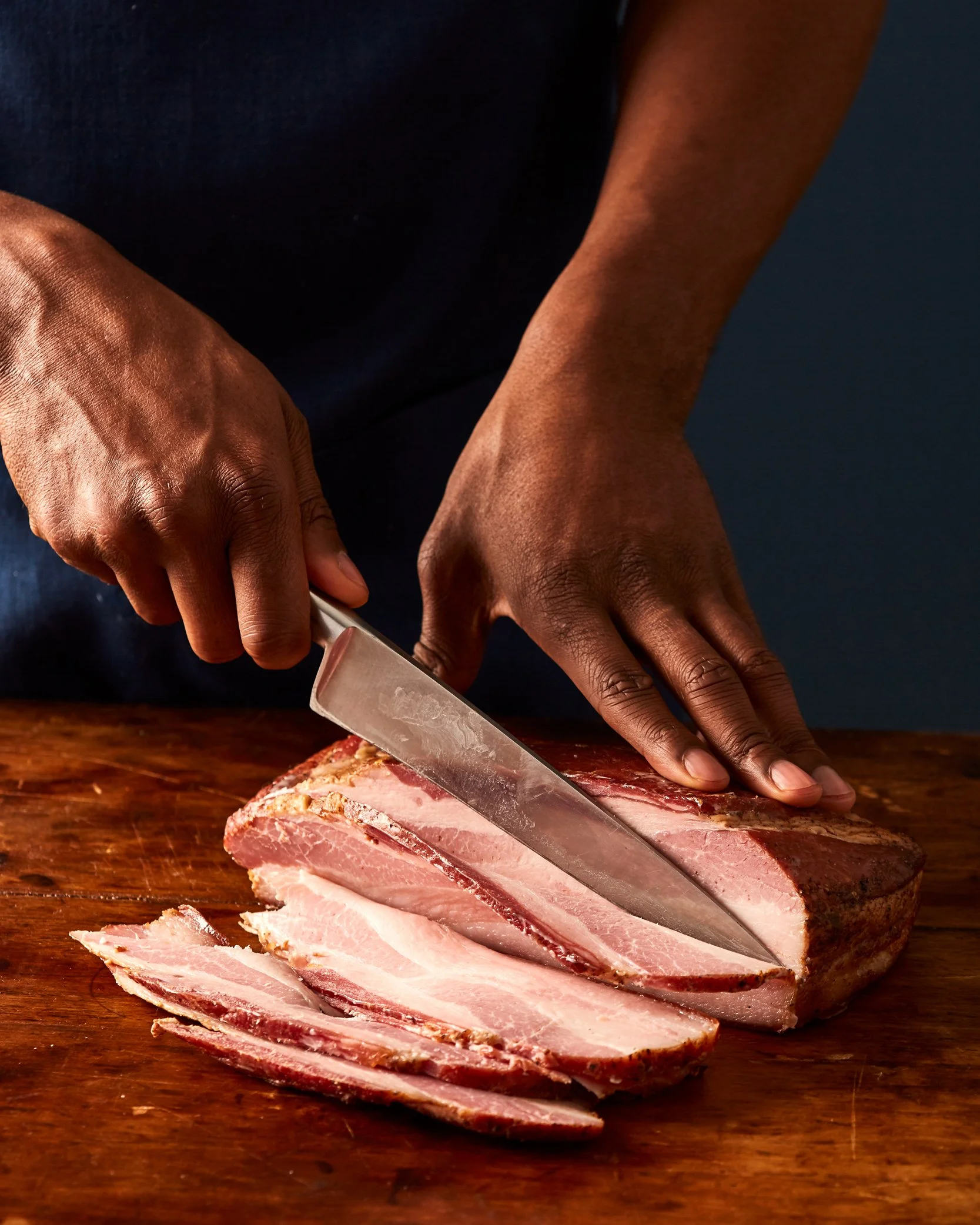 Hands slicing smoked bacon on a wood table. Boston based food and hospitality photographer.