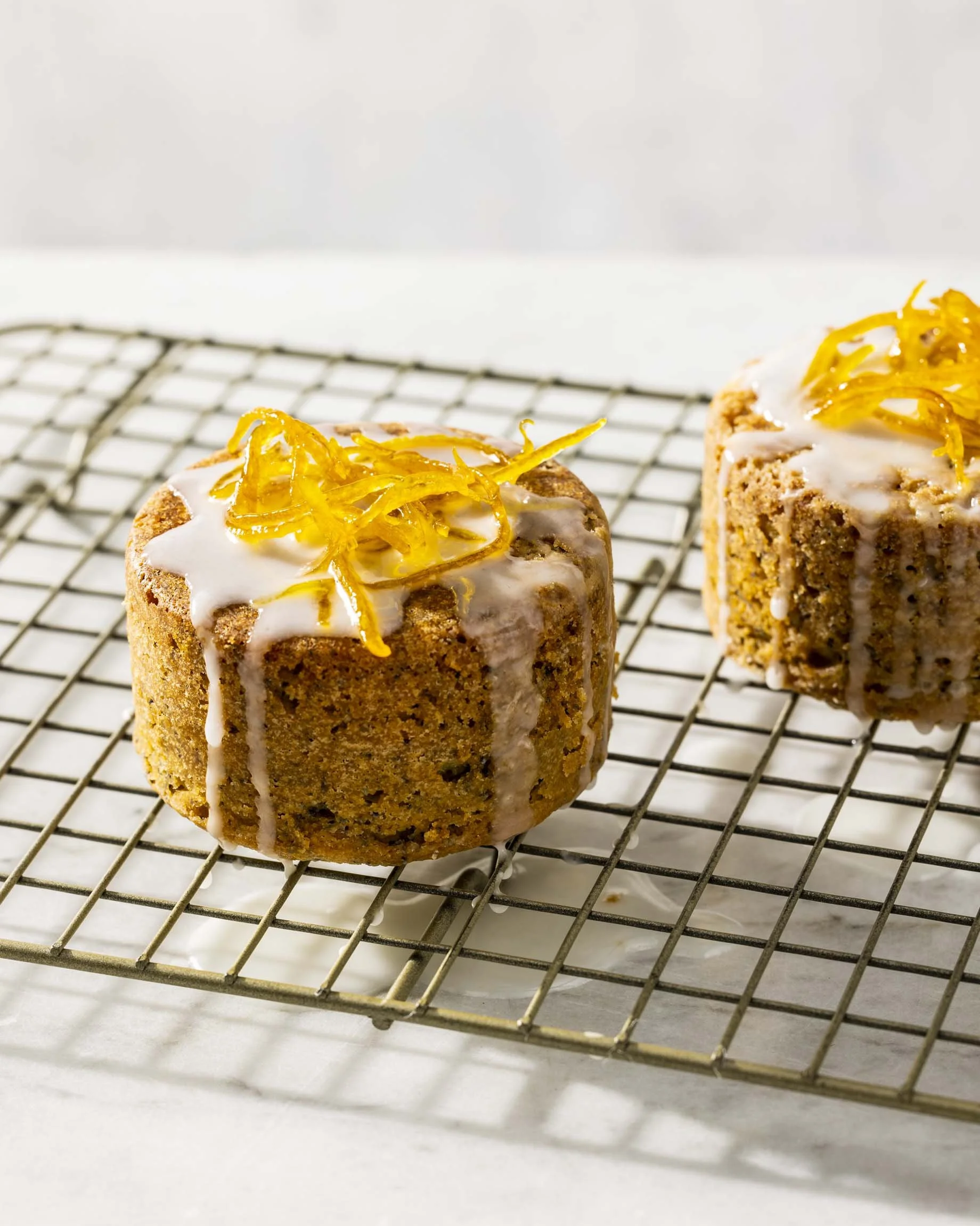 Two small, roundnut cakes topped with white icing and yellow candied citrus peel on a cooling rack. Boston food photographer.