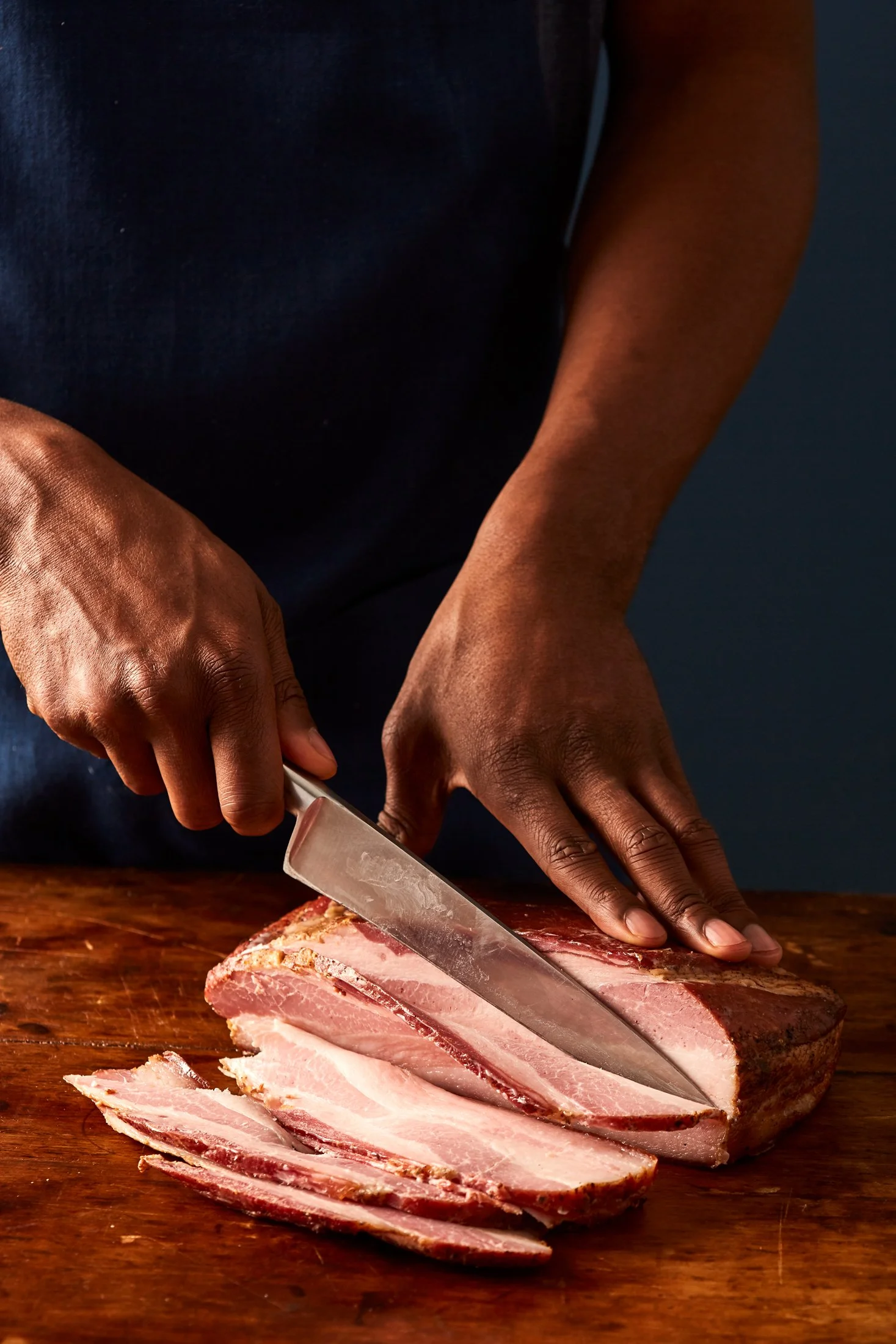 Person slicing cooked bacon on a wooden cutting board