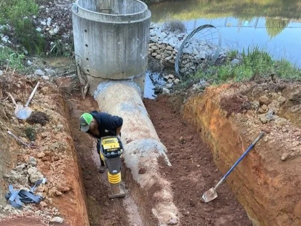 Hilton Head Stormwater Management crew member operates equipment to properly compact soil around a newly repaired retention pond pipe during a sinkhole repair project.