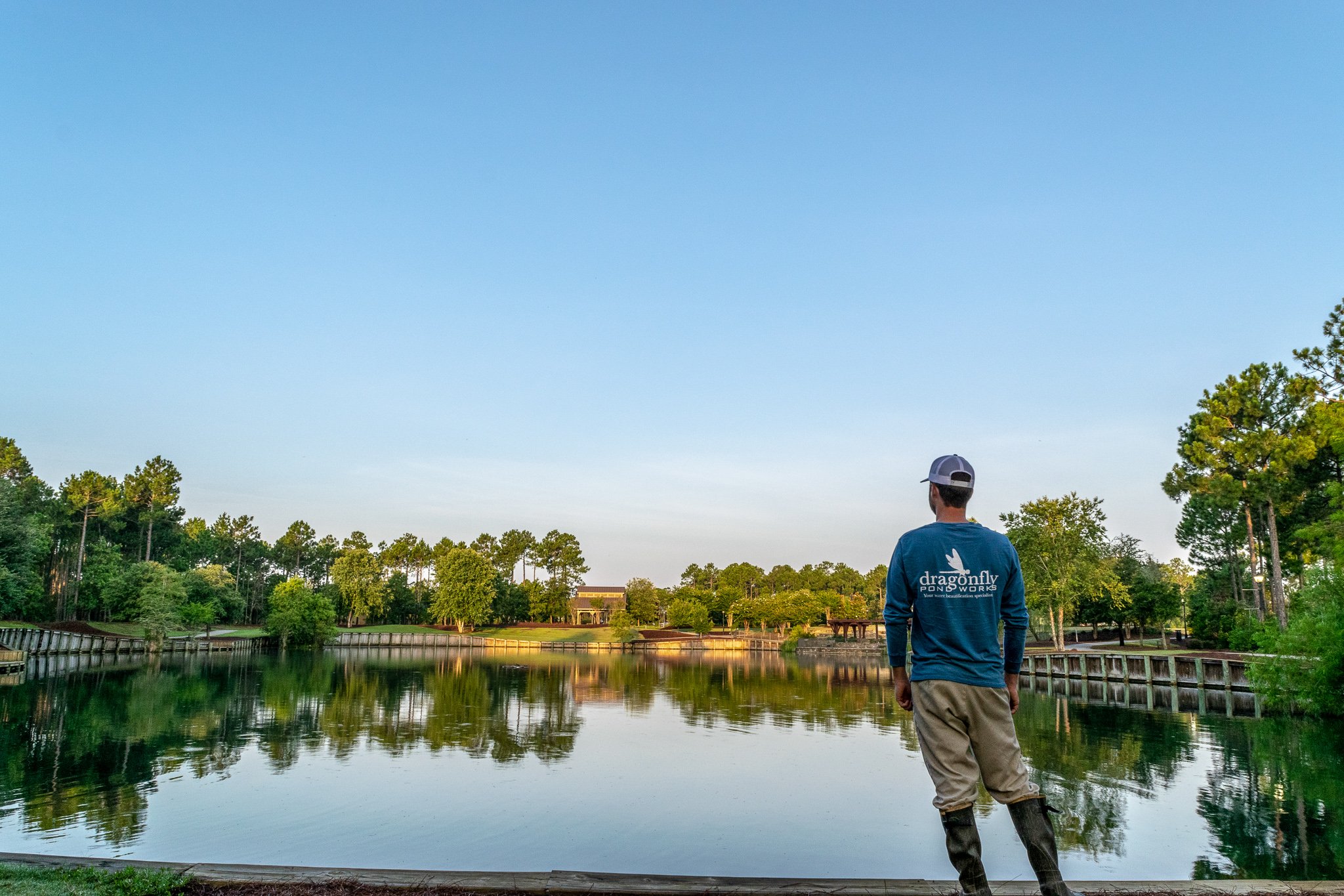 A Dragonfly stormwater pond maintenance tech stands in front of a retention pond after completing a routine maintenance visit.