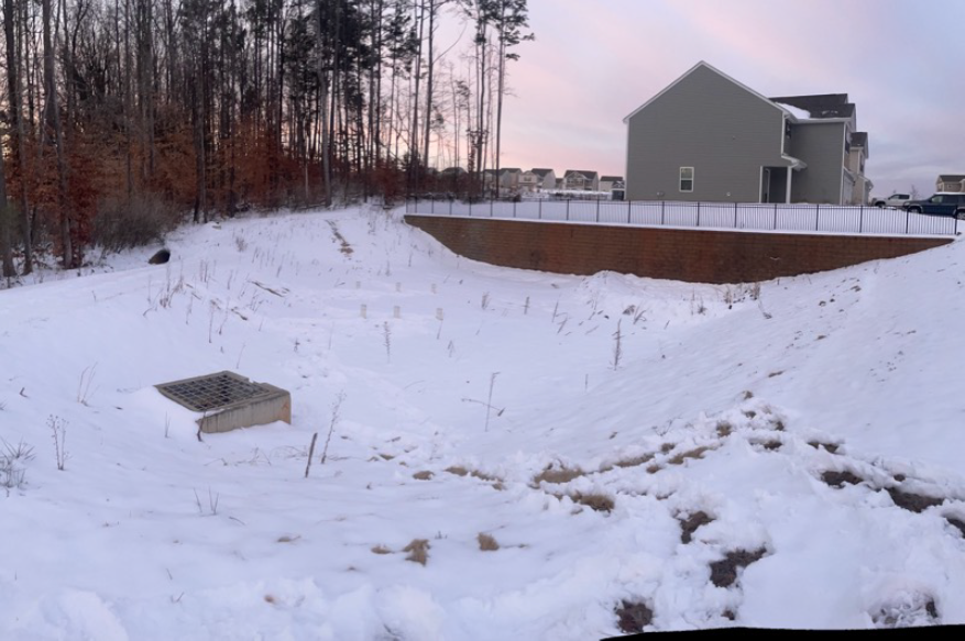 A community stormwater dry detention pond is full of snow and snow almost covers the riser.