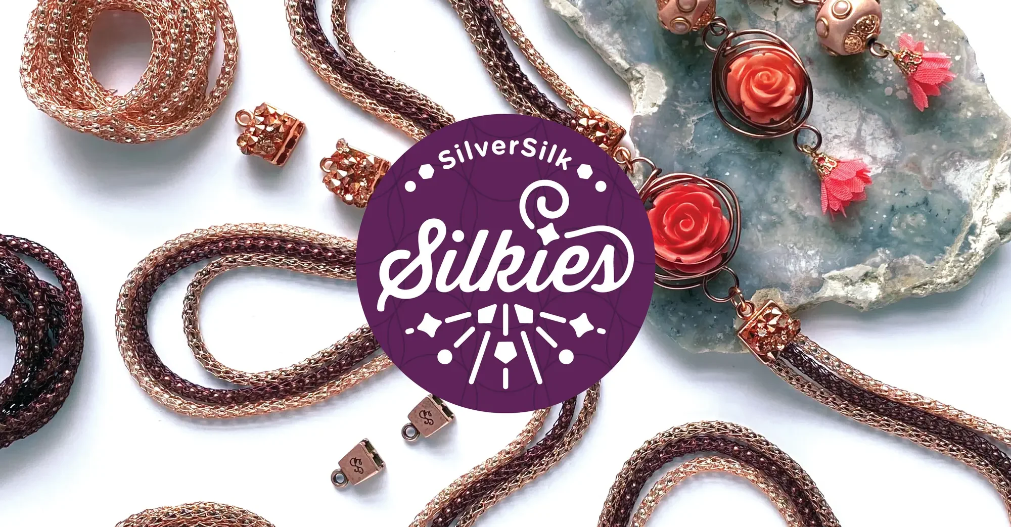 Various jewelry pieces including chains, earrings with coral roses, and decorative accessories displayed on a white surface, with a purple circle logo in the center reading "Silversilk Sukiés".