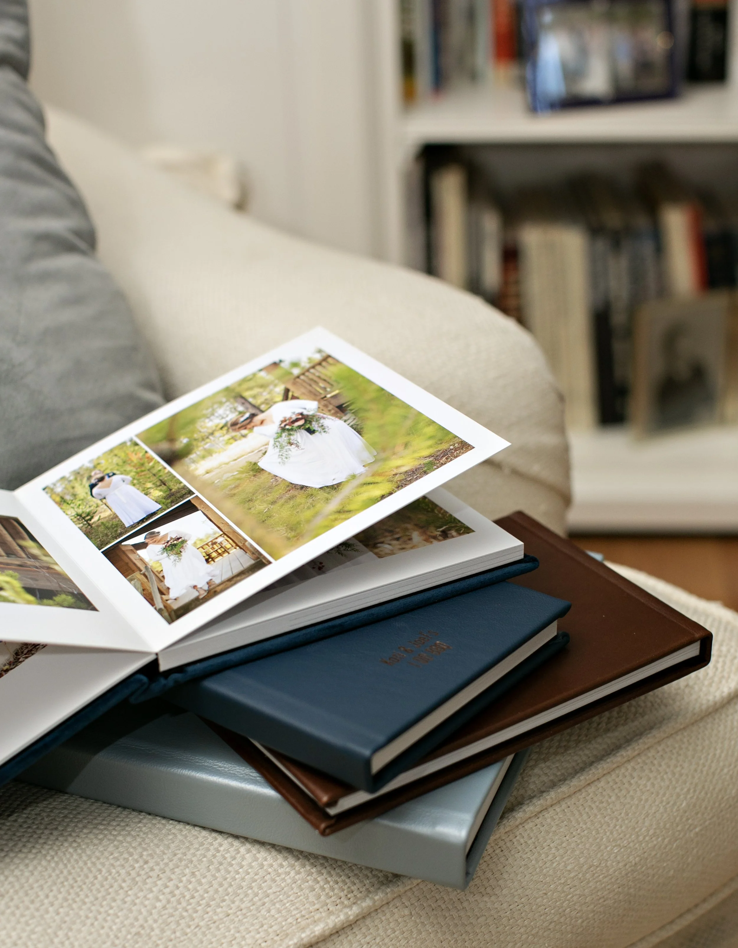 Photo of a wedding photo album open on a stack of books, sitting on a beige fabric surface, with a bookshelf in the background.