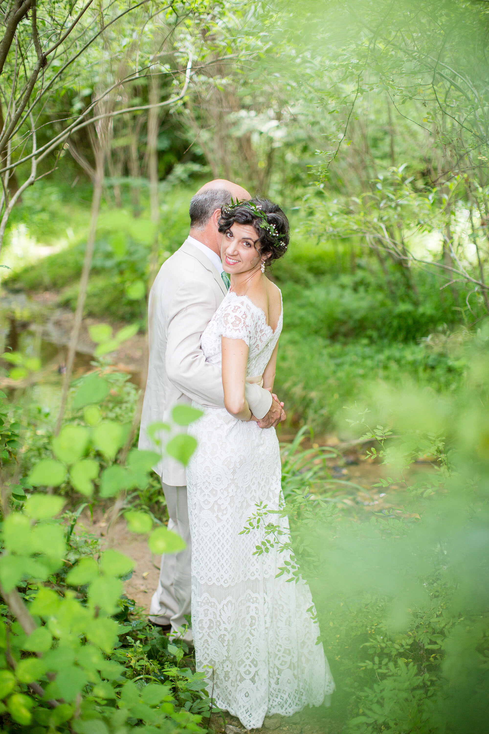  Bride and groom embracing in the forest, bride looking at the camera wearing custom handmade earrings 