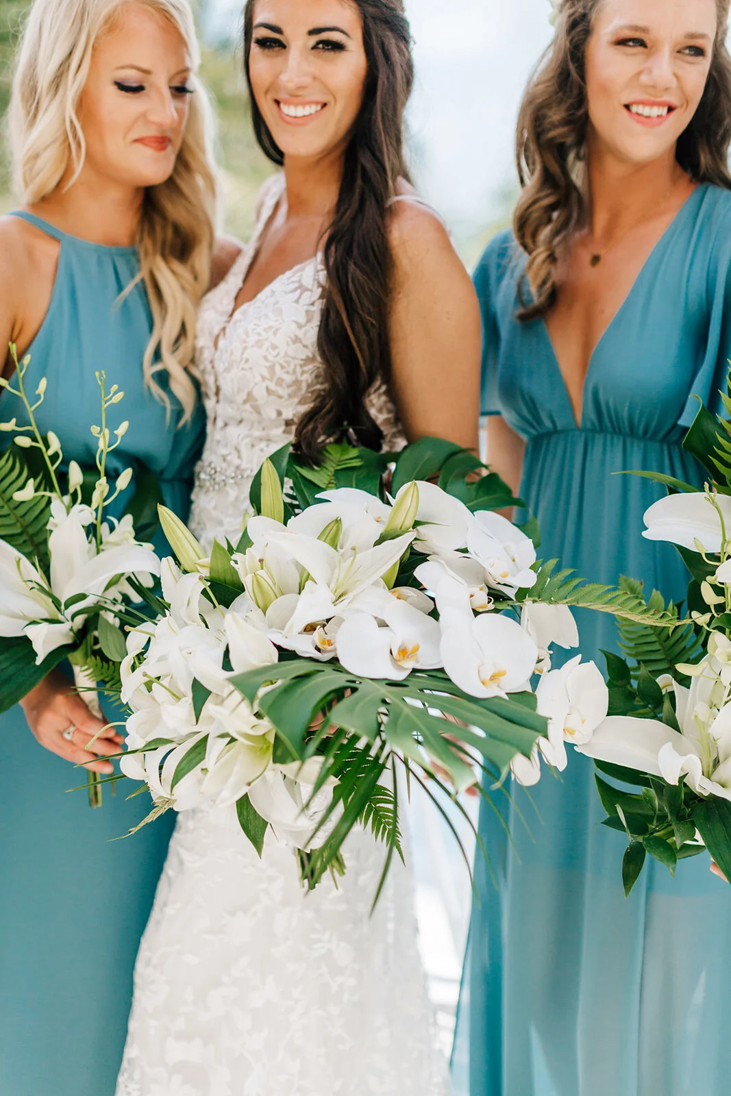 Bride with two bridesmaids in teal dresses holding bouquets of white flowers and green leaves