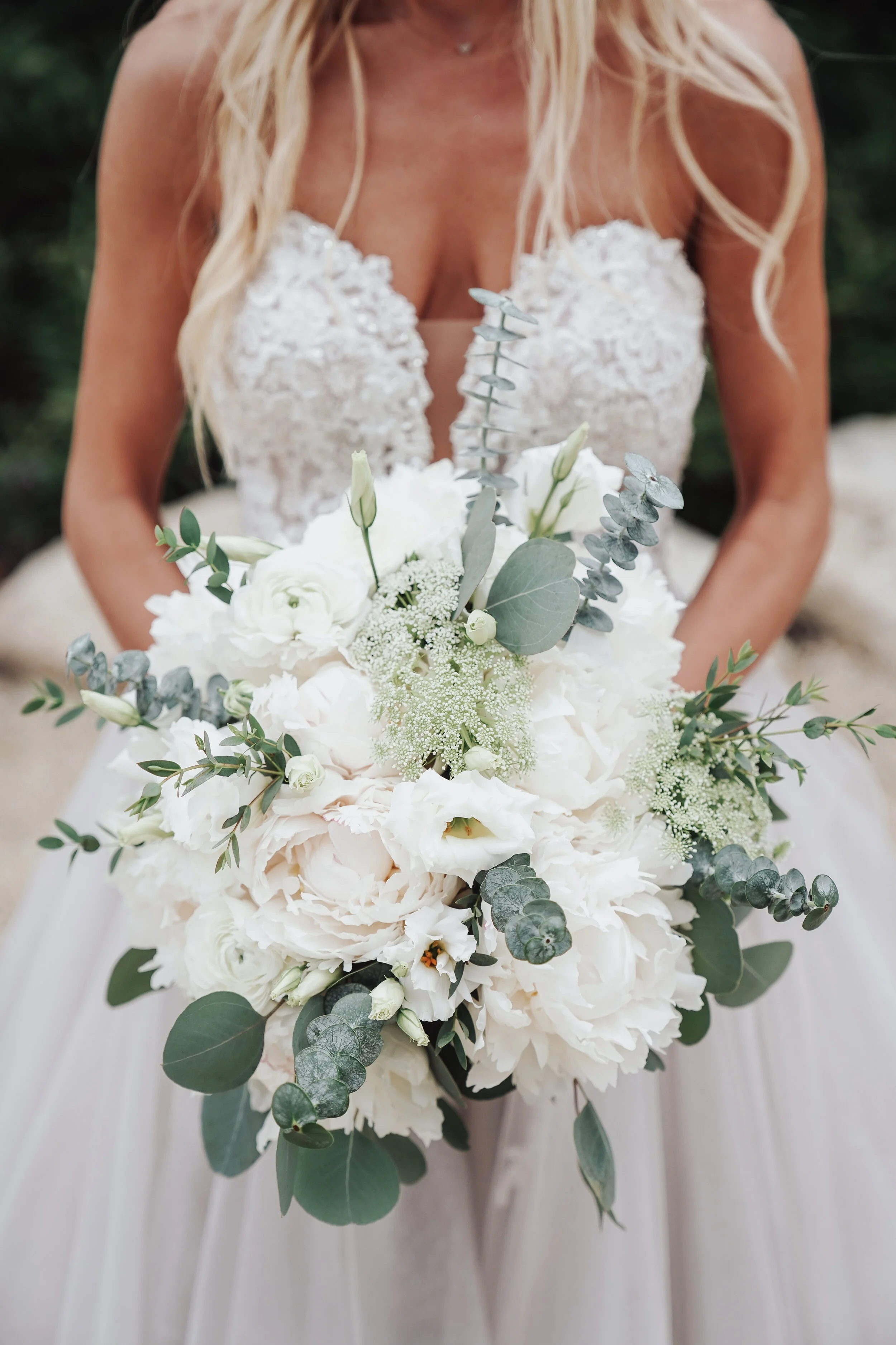 Bride holding a bouquet of white flowers and greenery in a wedding dress
