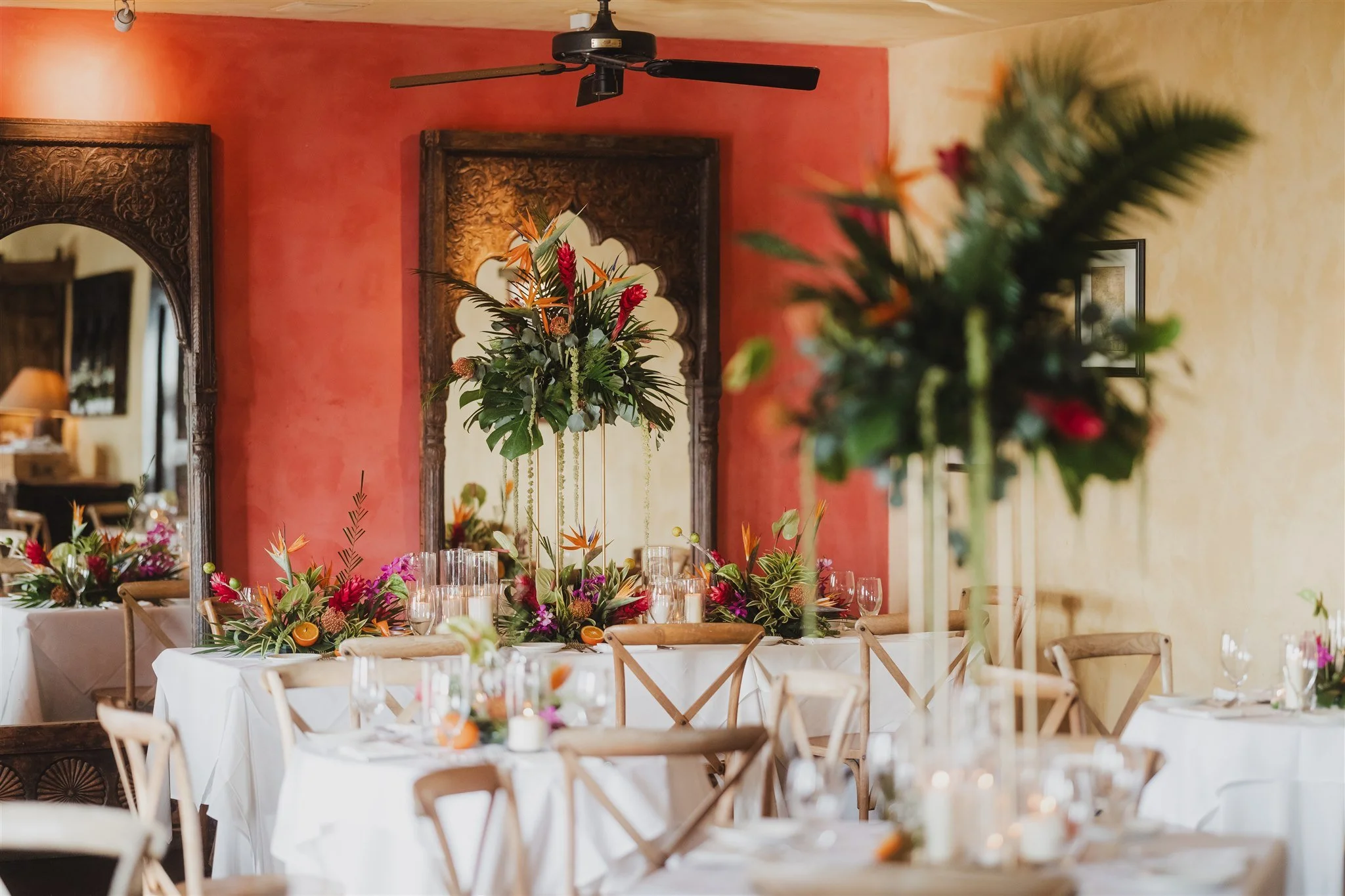 Elegant dining room with tropical floral centerpieces, wooden chairs, and white tablecloths.