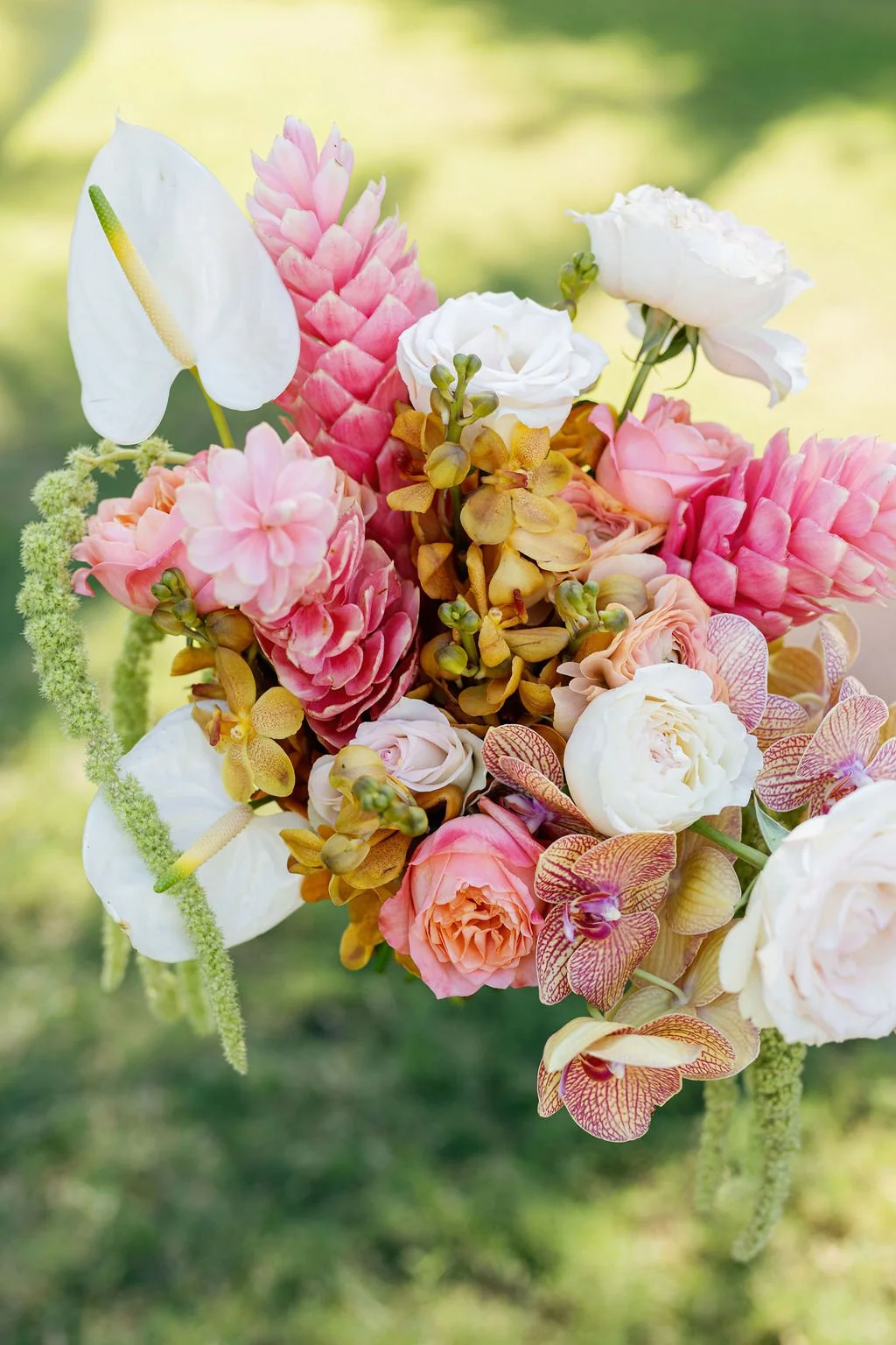 A vibrant bouquet of various flowers including white anthuriums, pink cluster flowers, white peonies, and orchids, with a blurred green background.