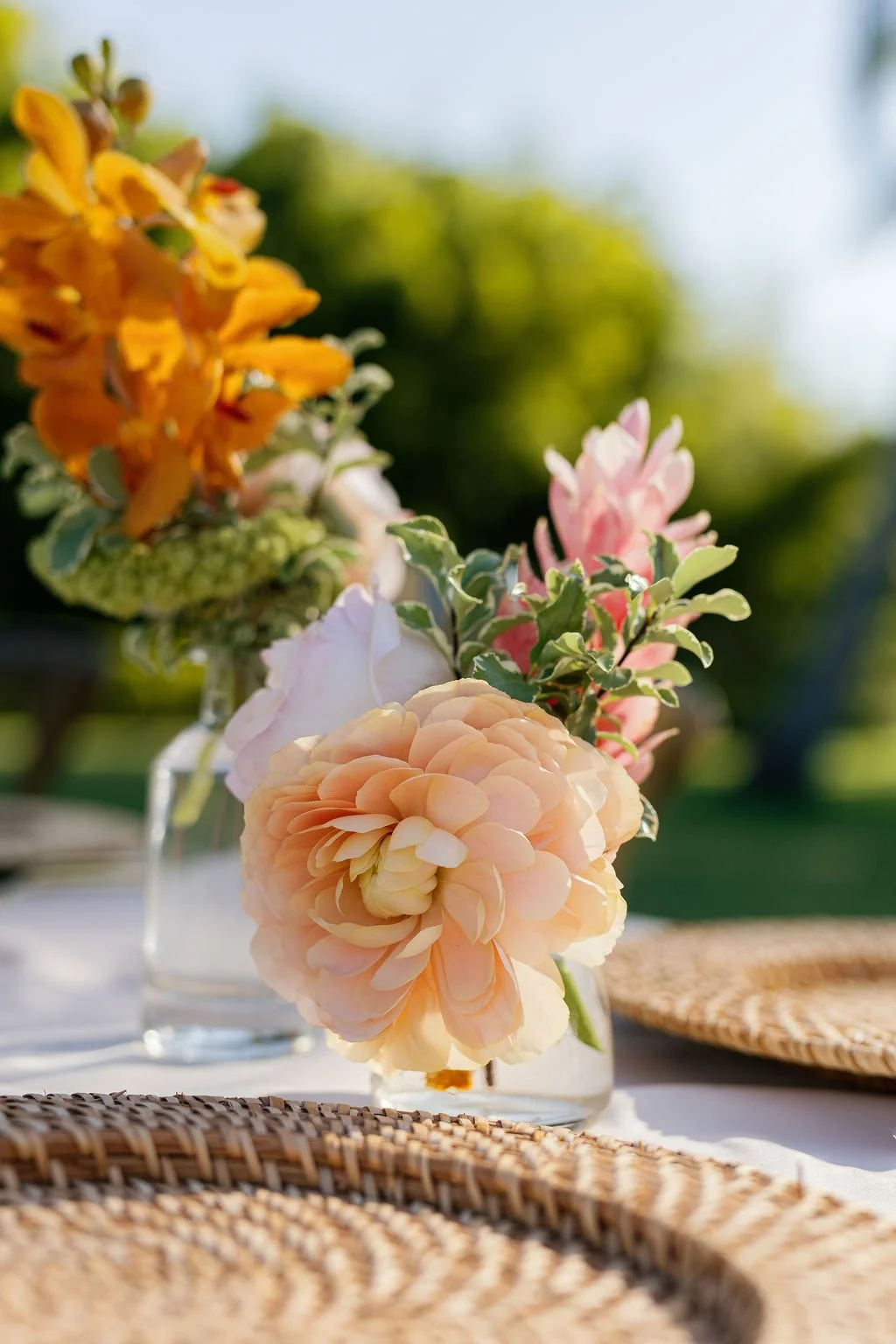 A close-up of a bouquet of pink and peach peonies in a glass vase on a table outdoors.