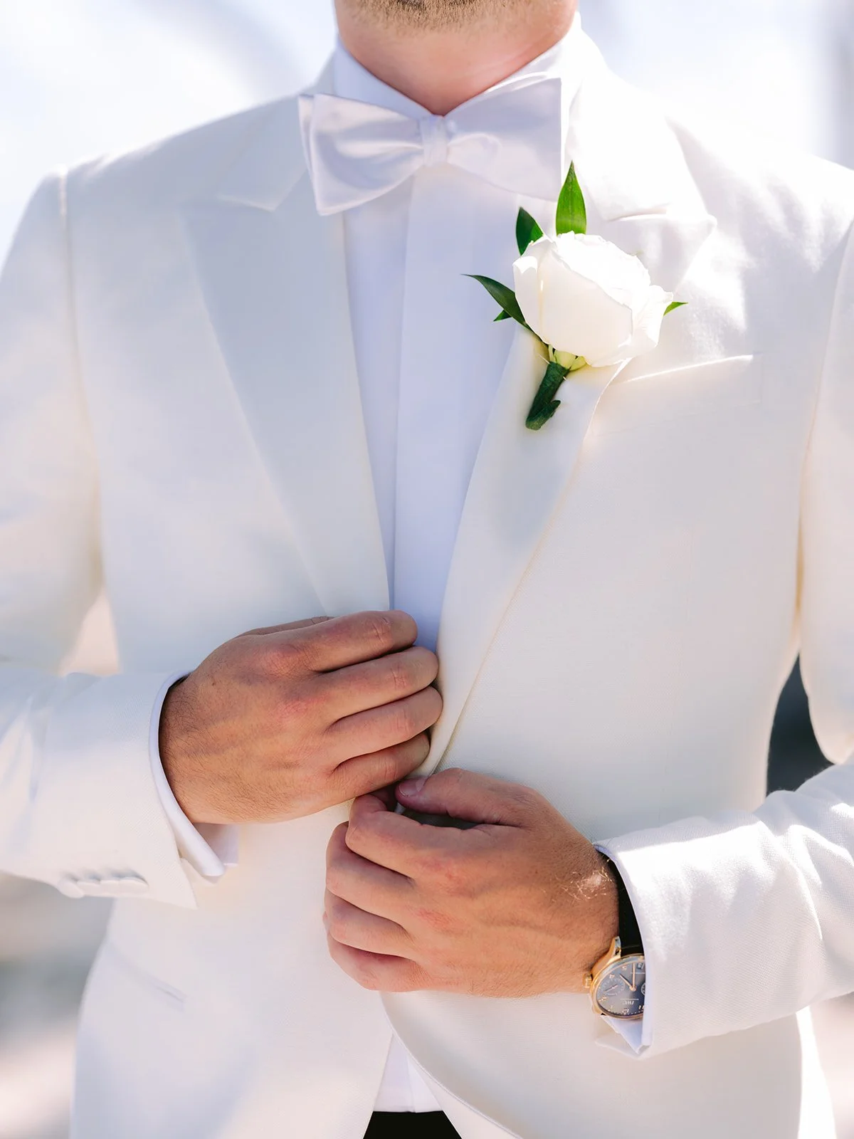 Man in white suit with boutonniere adjusting jacket