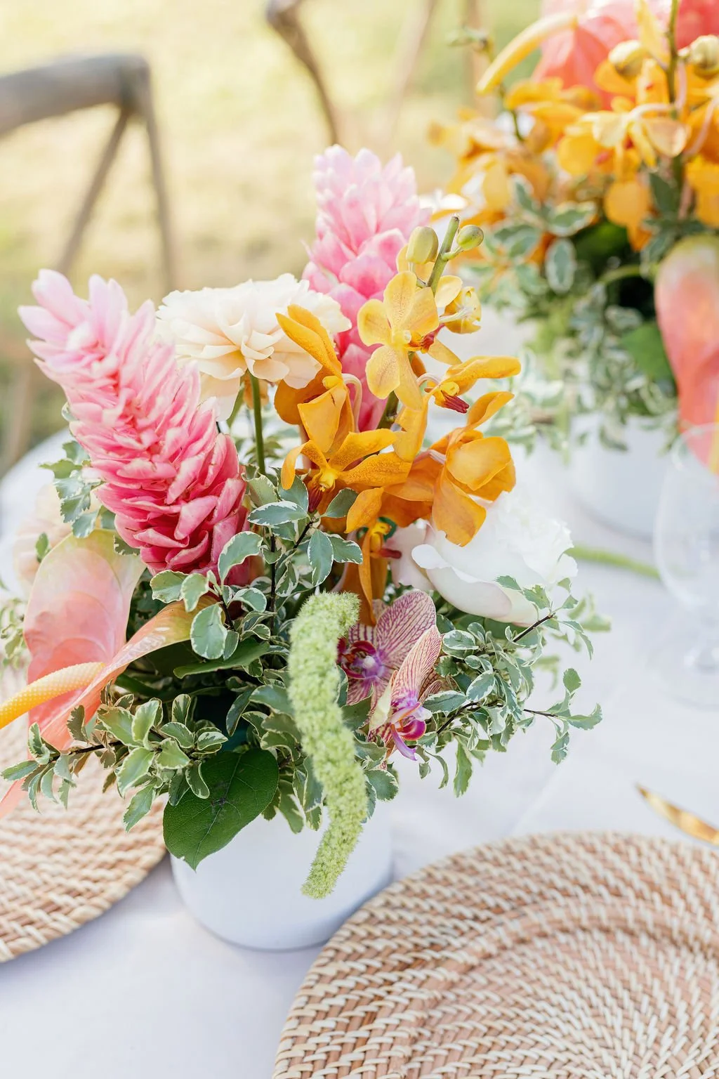 Colorful flower arrangement with pink, yellow, white, and purple flowers on a white table with woven placemats.