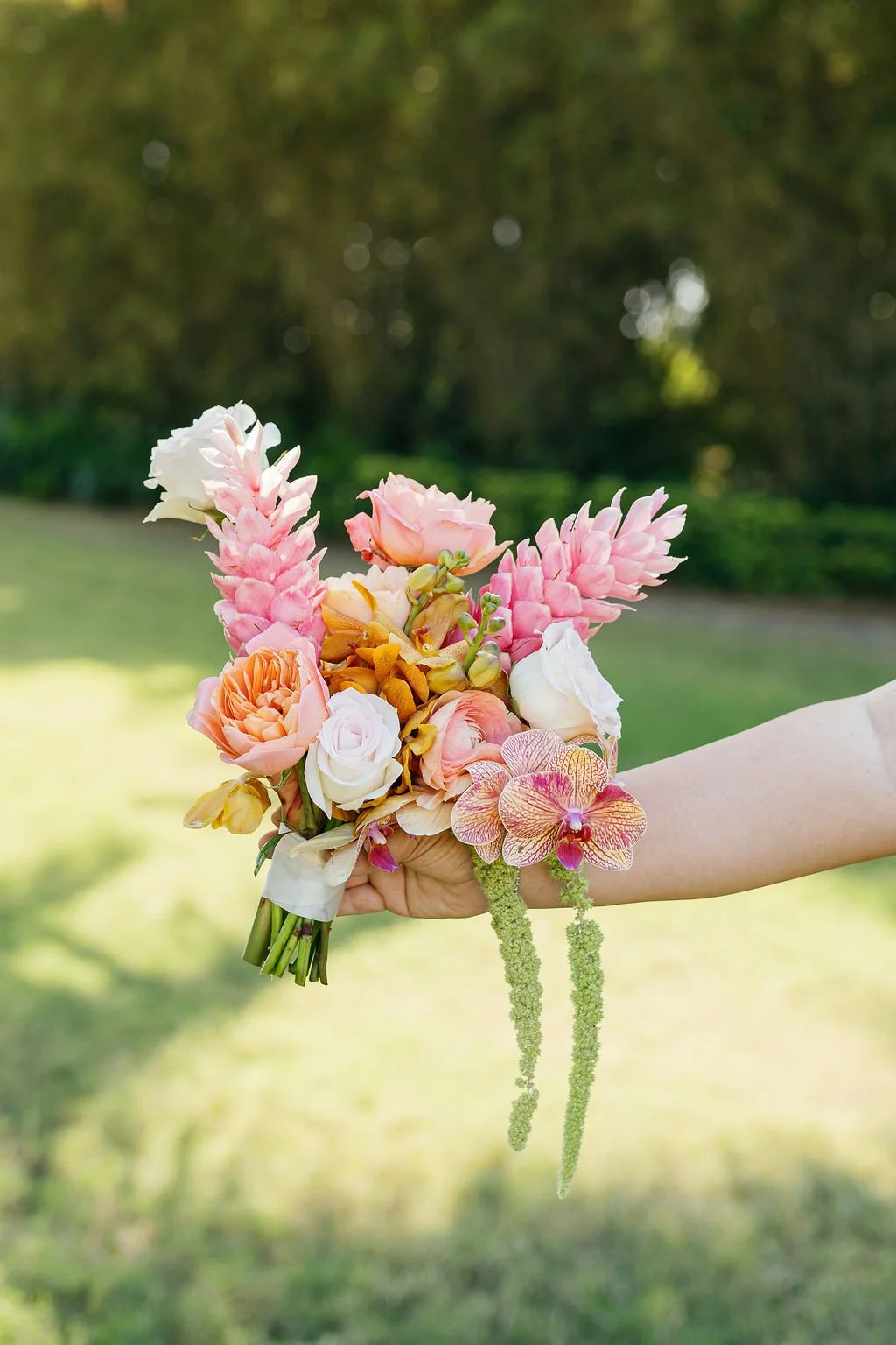 A hand holding a colorful bouquet of flowers outdoors, with a blurred green background.