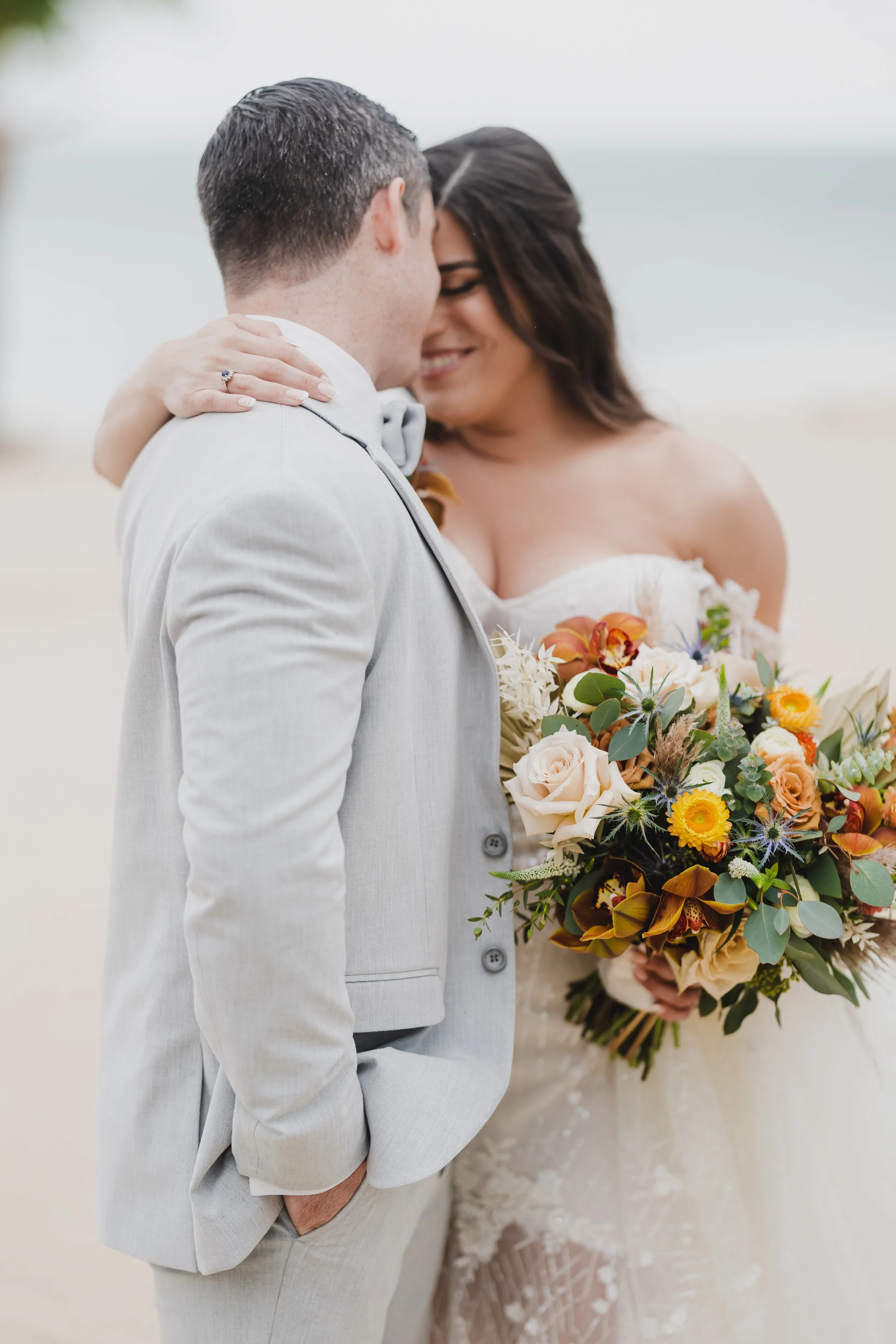 Bride and groom embracing with bouquet on beach