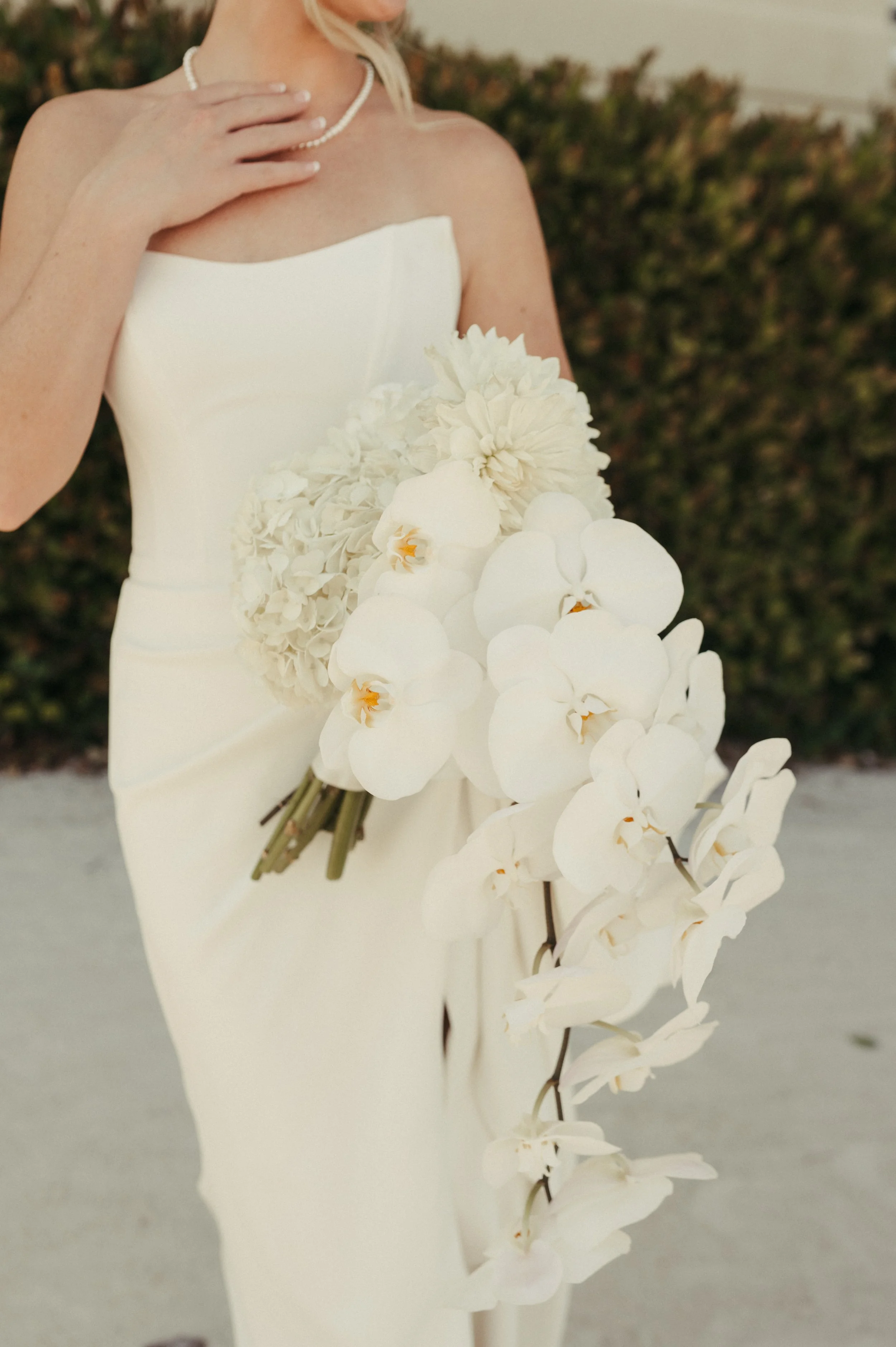 Bride in white dress holding bouquet of white orchids and flowers.