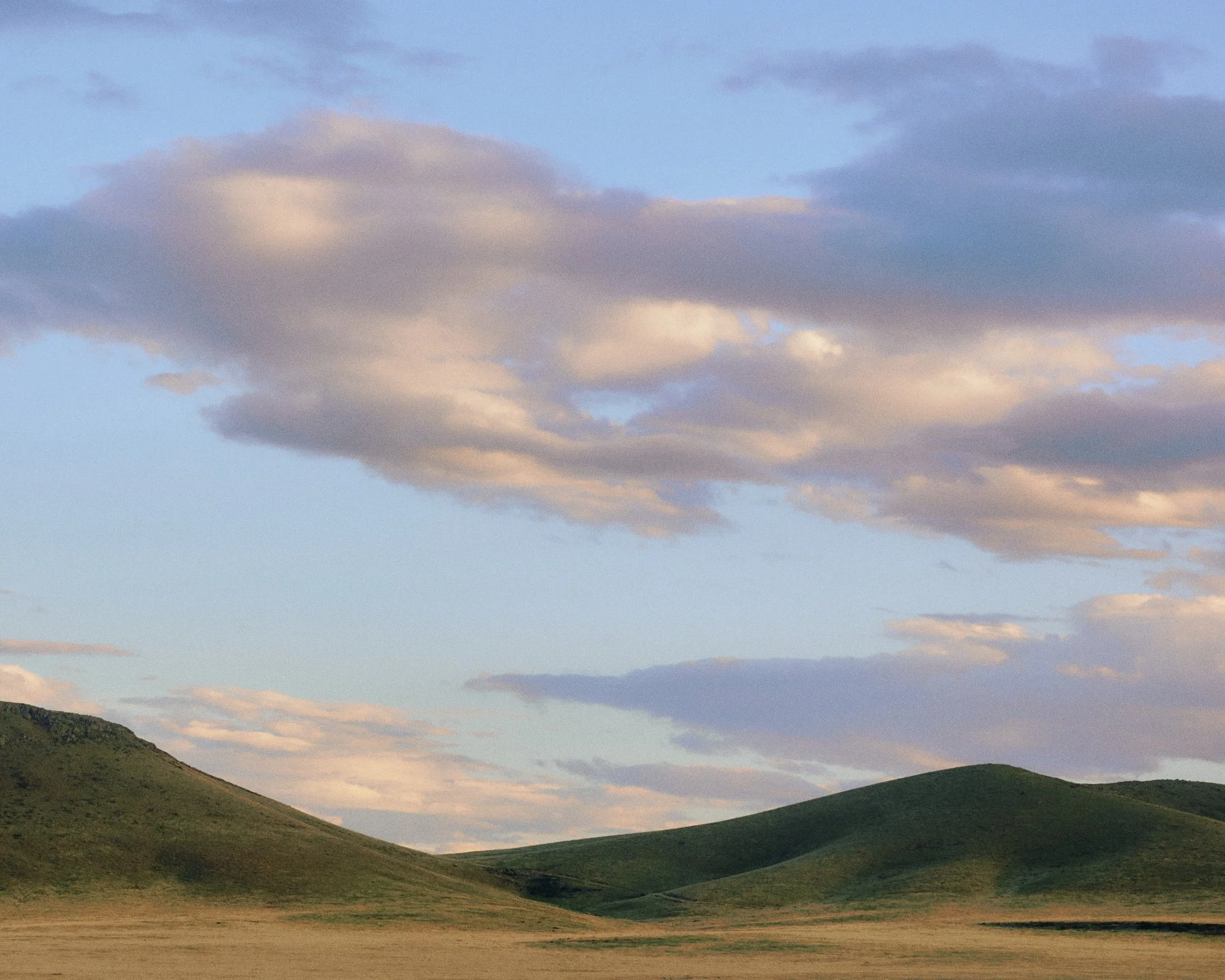 Green rolling hills under a partly cloudy sky during daytime.