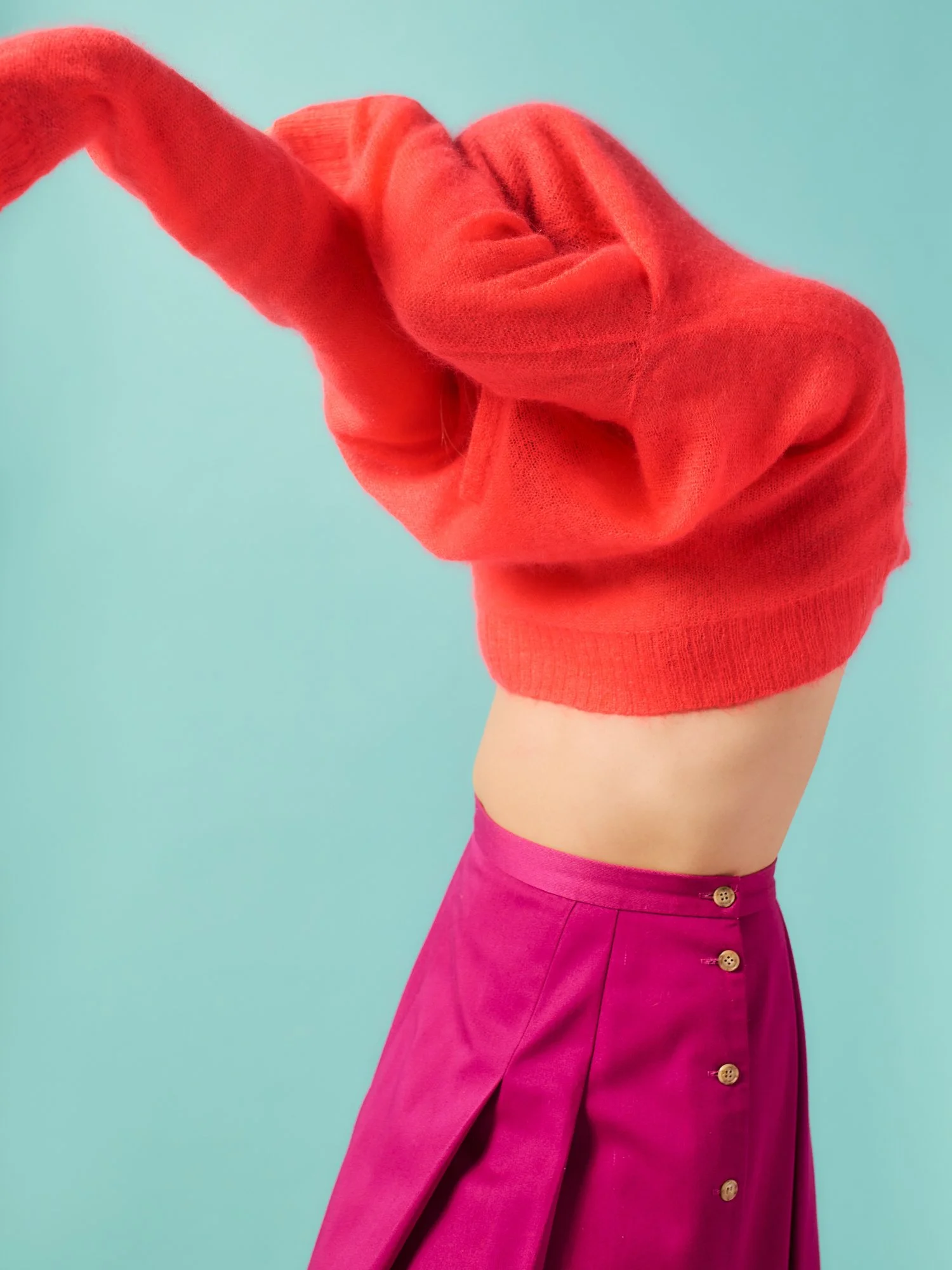 Close-up of a person wearing a red sweater and a pink high-waisted skirt with button details, against a light blue background.