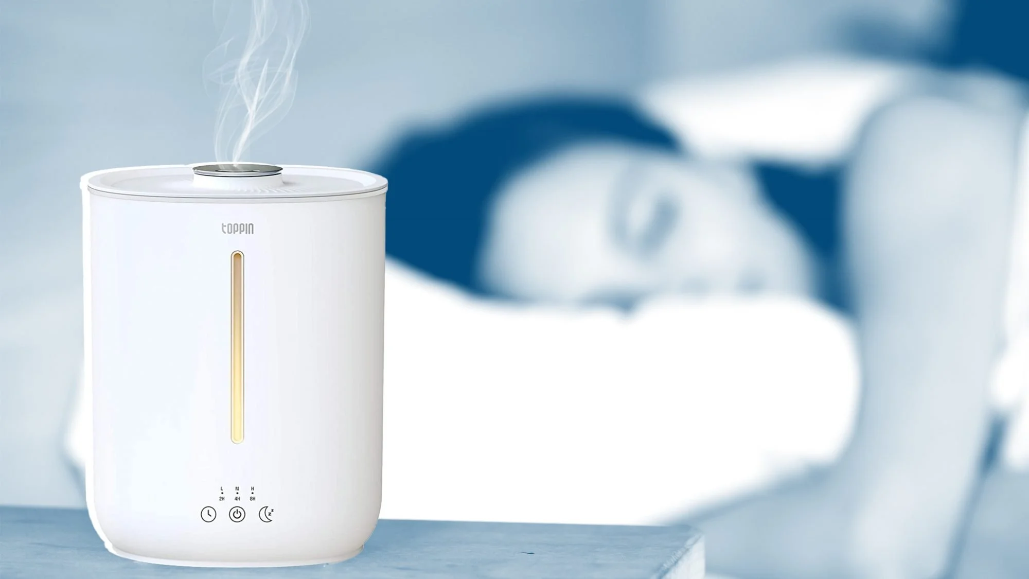 White humidifier emitting vapor on a table, blurred background of a sleeping person.