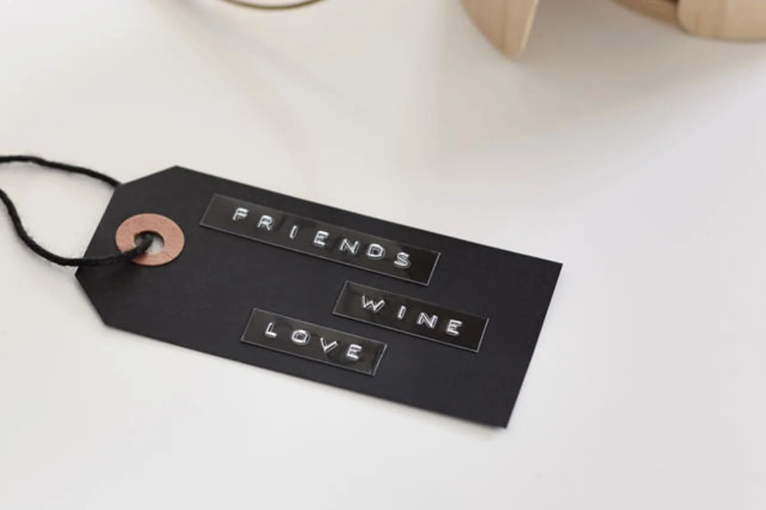 Black gift tag with embossed words: Friends, Wine, Love, on white surface.