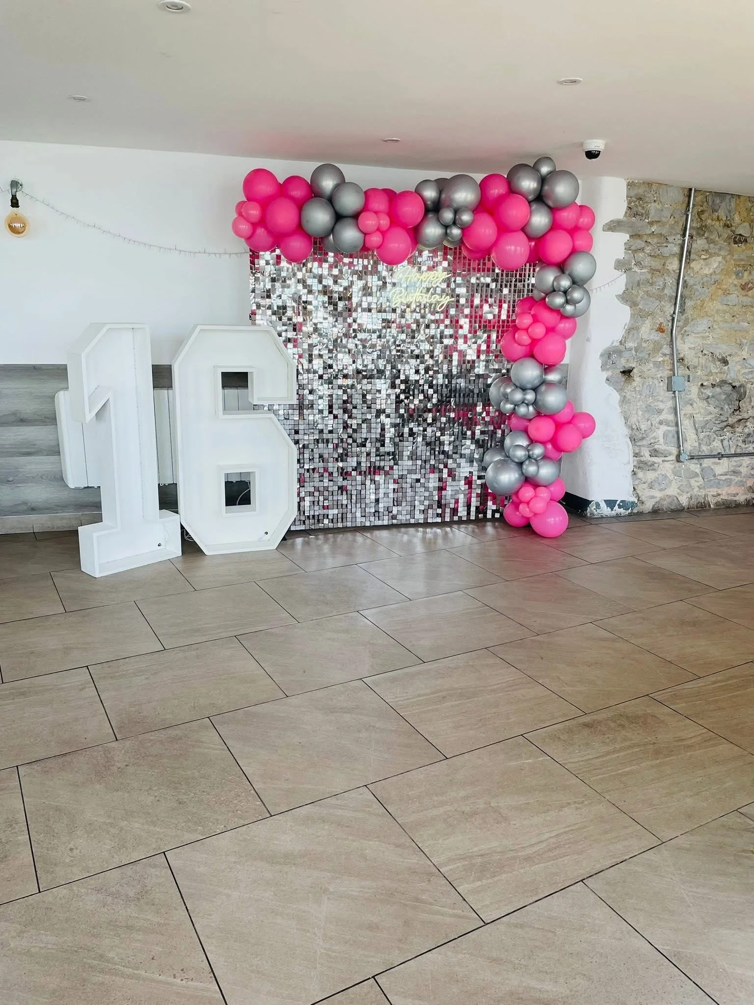 Decorative background with pink and silver balloons, a large white number 16, and a shiny silver and mirrored backdrop indicating a 16th birthday celebration.