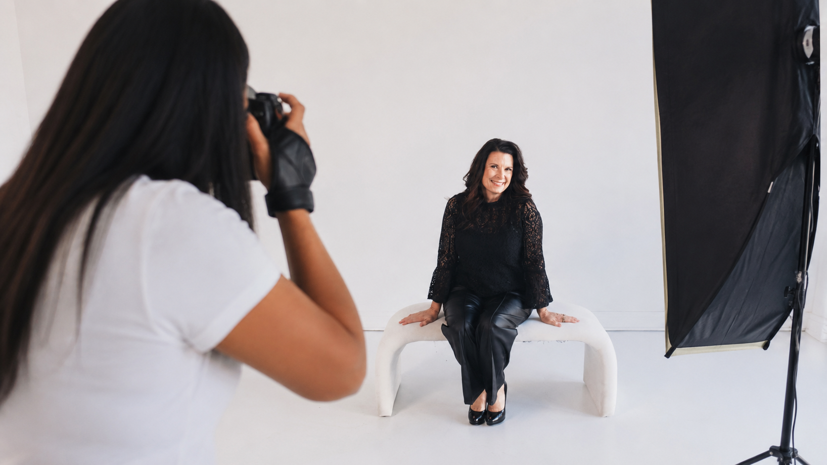 Woman in black lace top and leather pants posing for a photo in a photography studio.