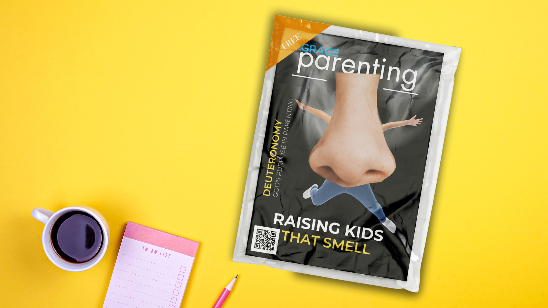 A fake parenting magazine cover titled "Raising Kids That Smell" with a close-up nose photo, wrapped in cellophane and staged on a yellow desk with coffee and a notepad.