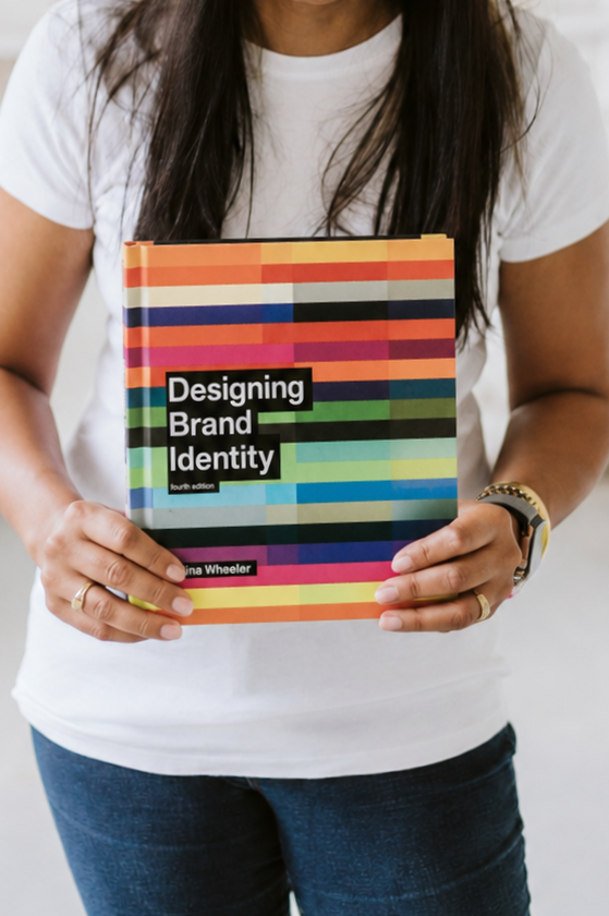 Person holding a book titled "Designing Brand Identity" with a colorful striped cover.