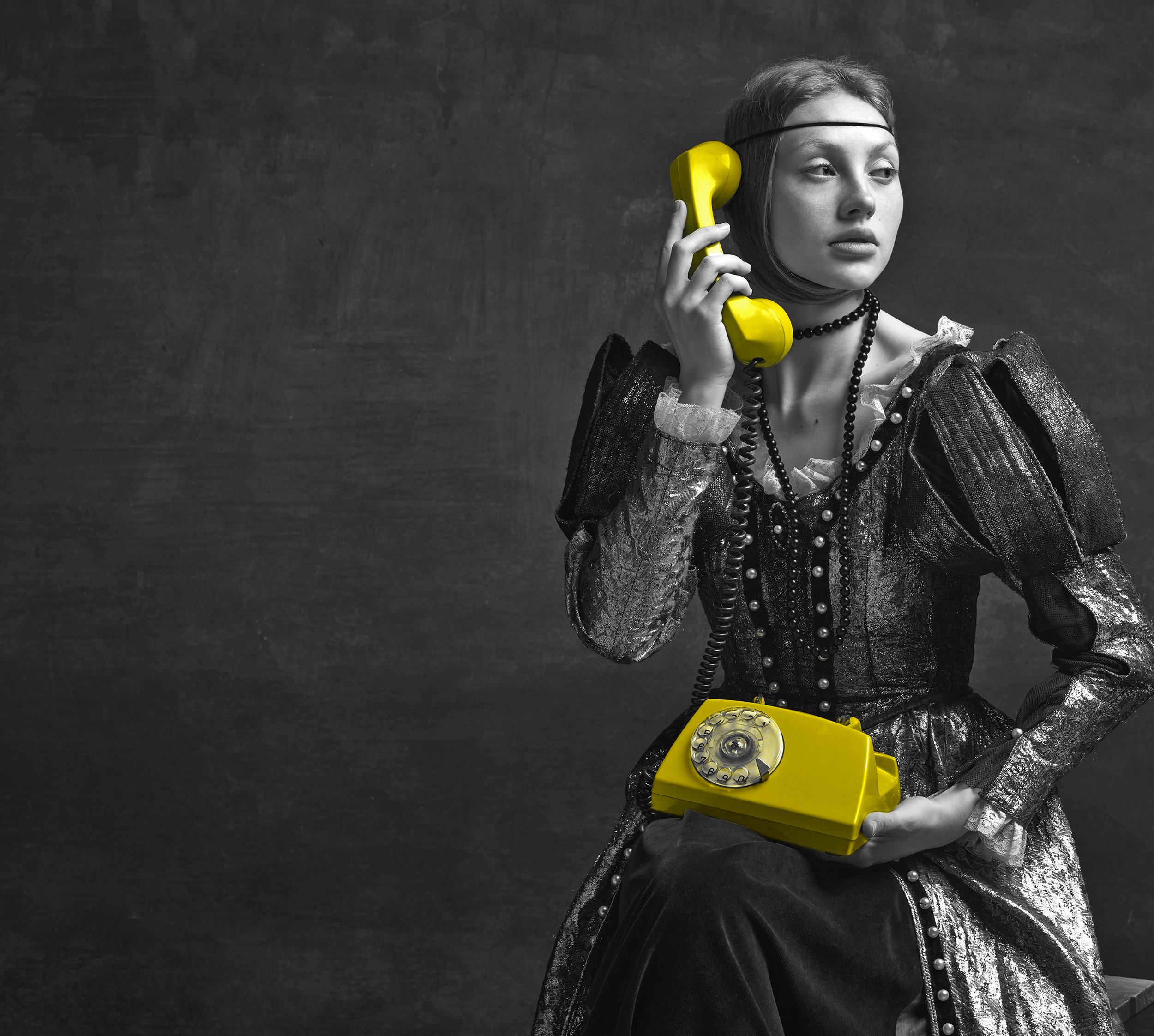 Black and white image of a woman in vintage attire holding a bright yellow rotary phone.