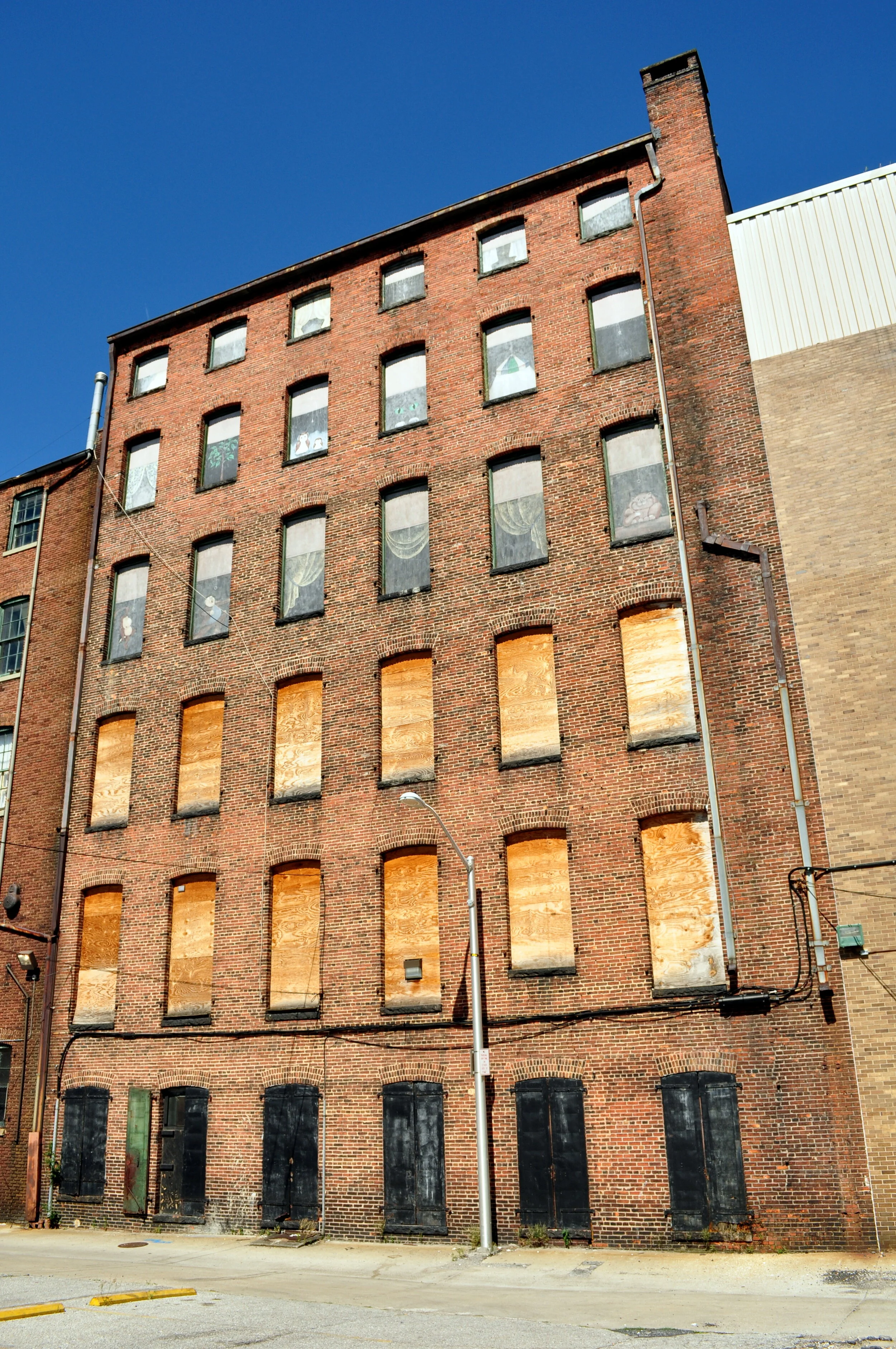 An old brick building with boarded-up windows on the ground and middle floors and some decorated windows on the top floor, under a clear blue sky.