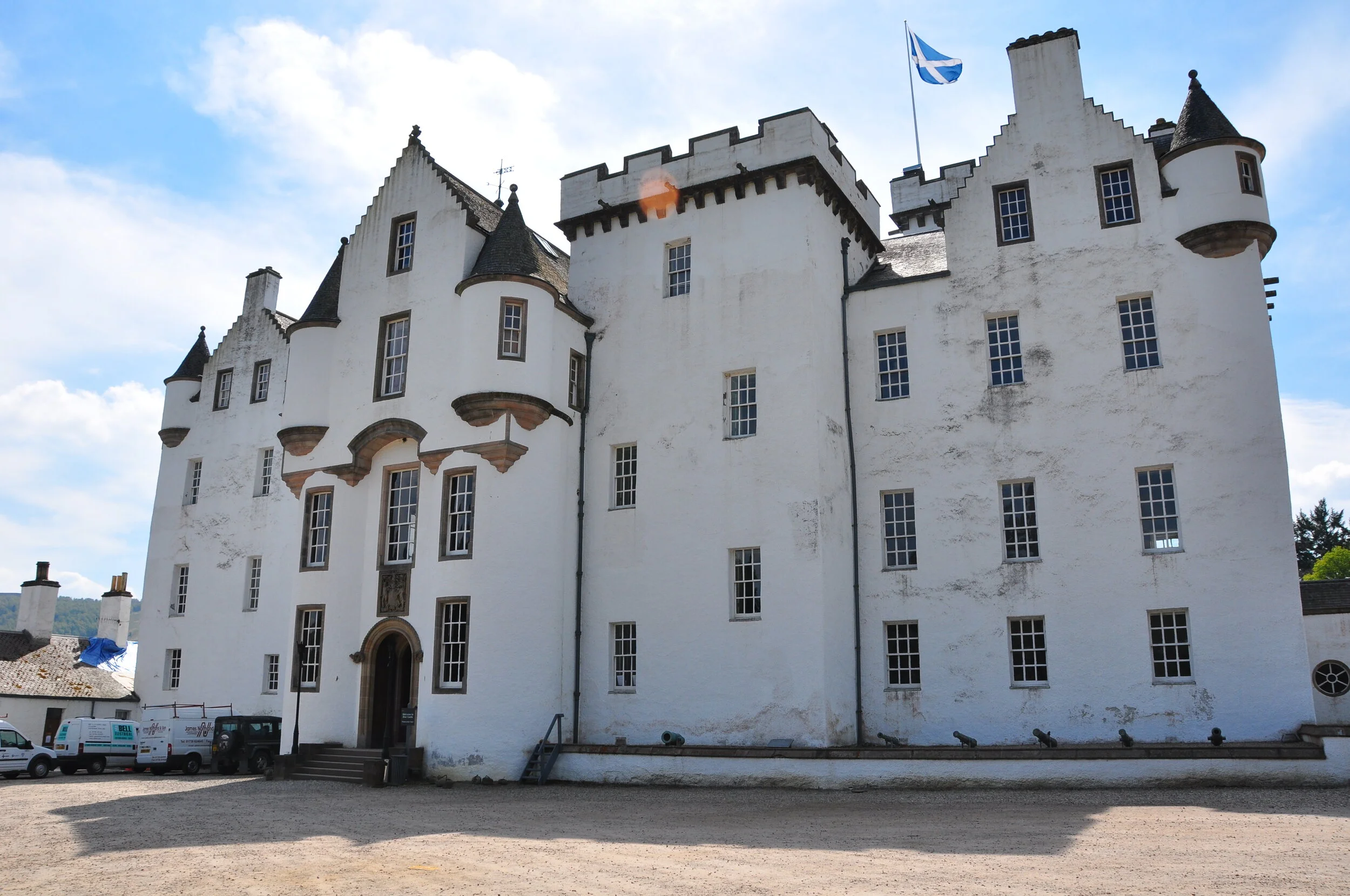 A large white castle with multiple turrets, windows, and a Scottish flag on top, set against a partly cloudy sky.