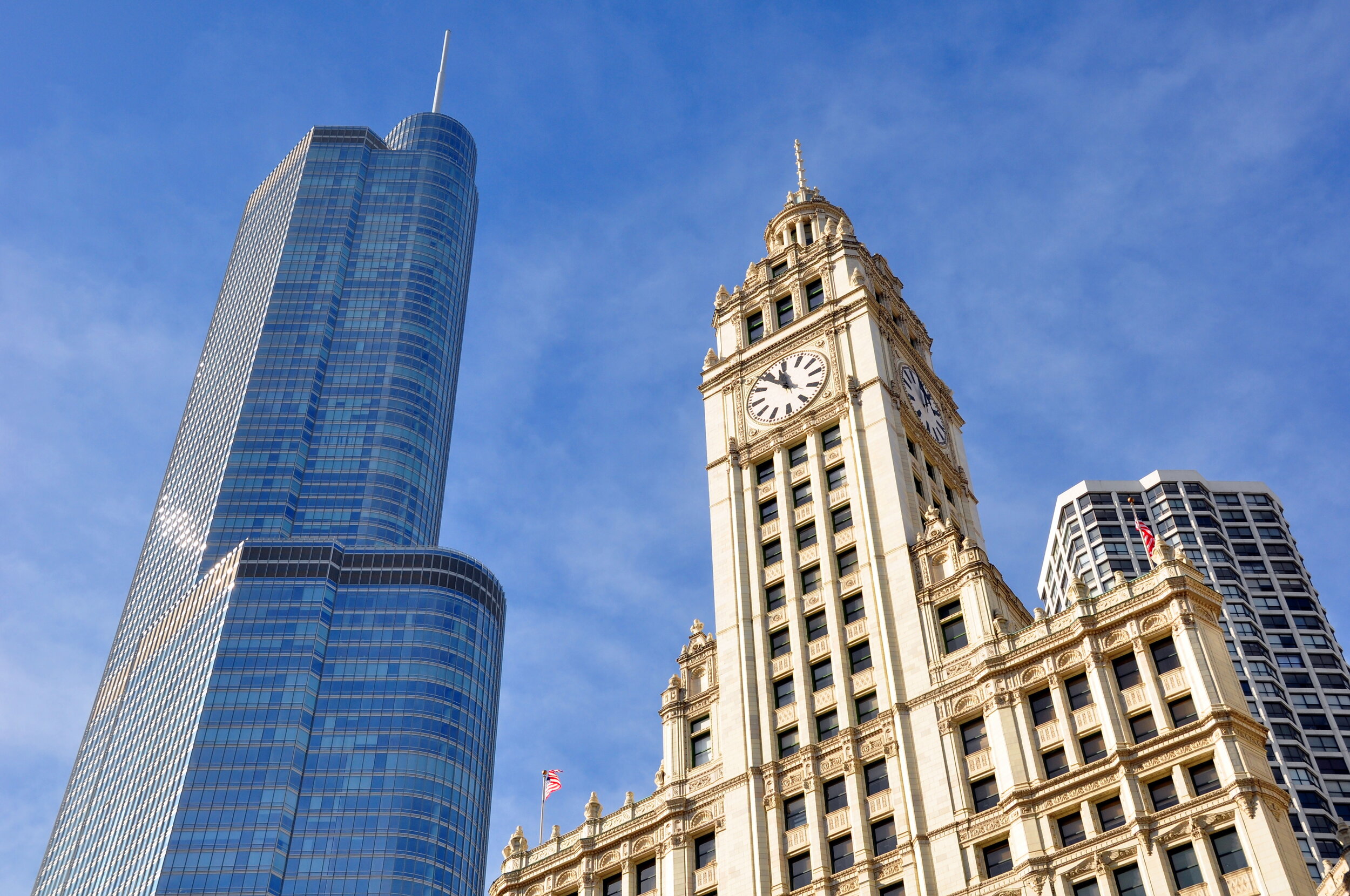 Skyscraper next to an ornate clock tower with a clear blue sky in the background.